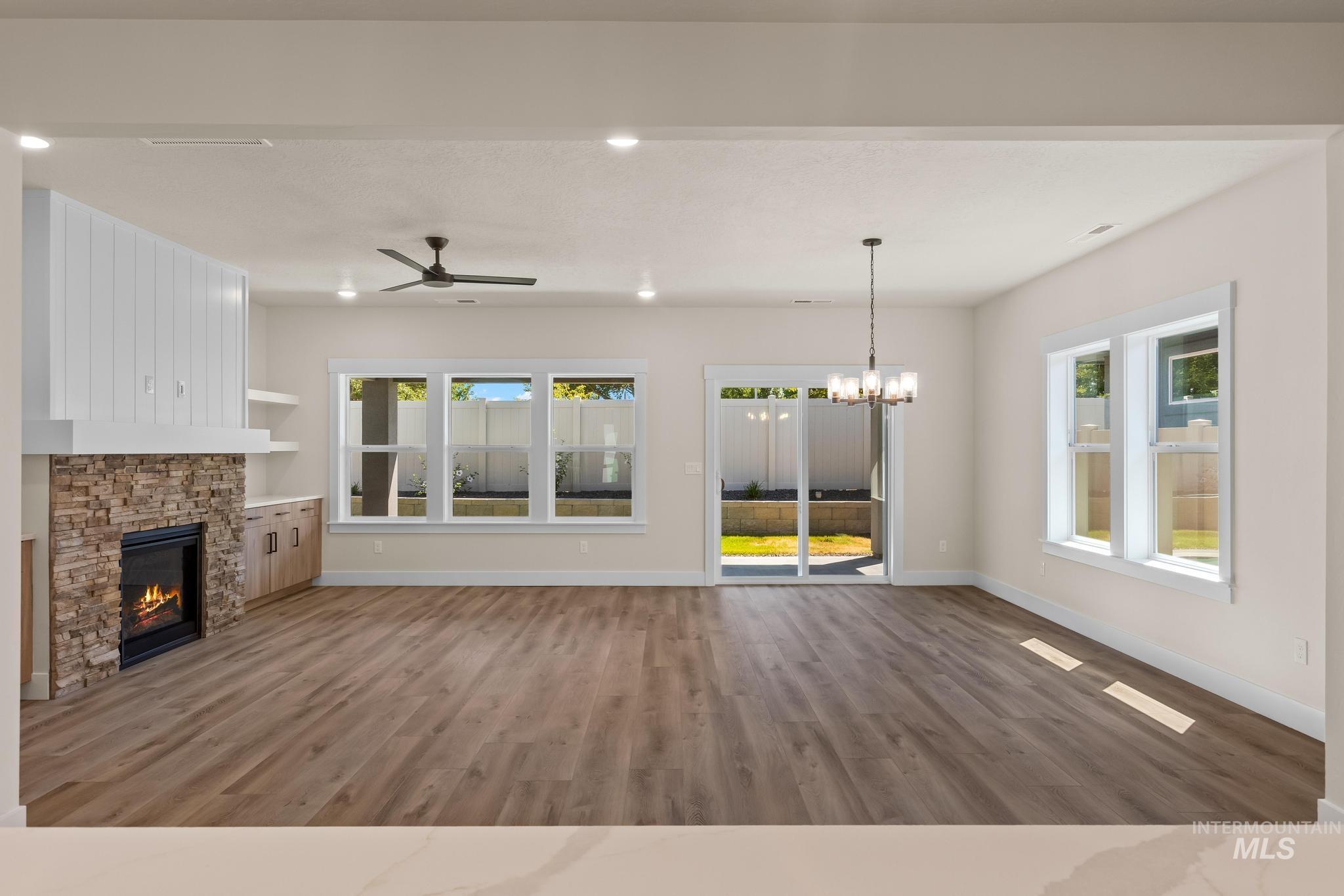 Unfurnished living room featuring light wood-type flooring, a stone fireplace, a chandelier, ceiling fan, and recessed lighting
