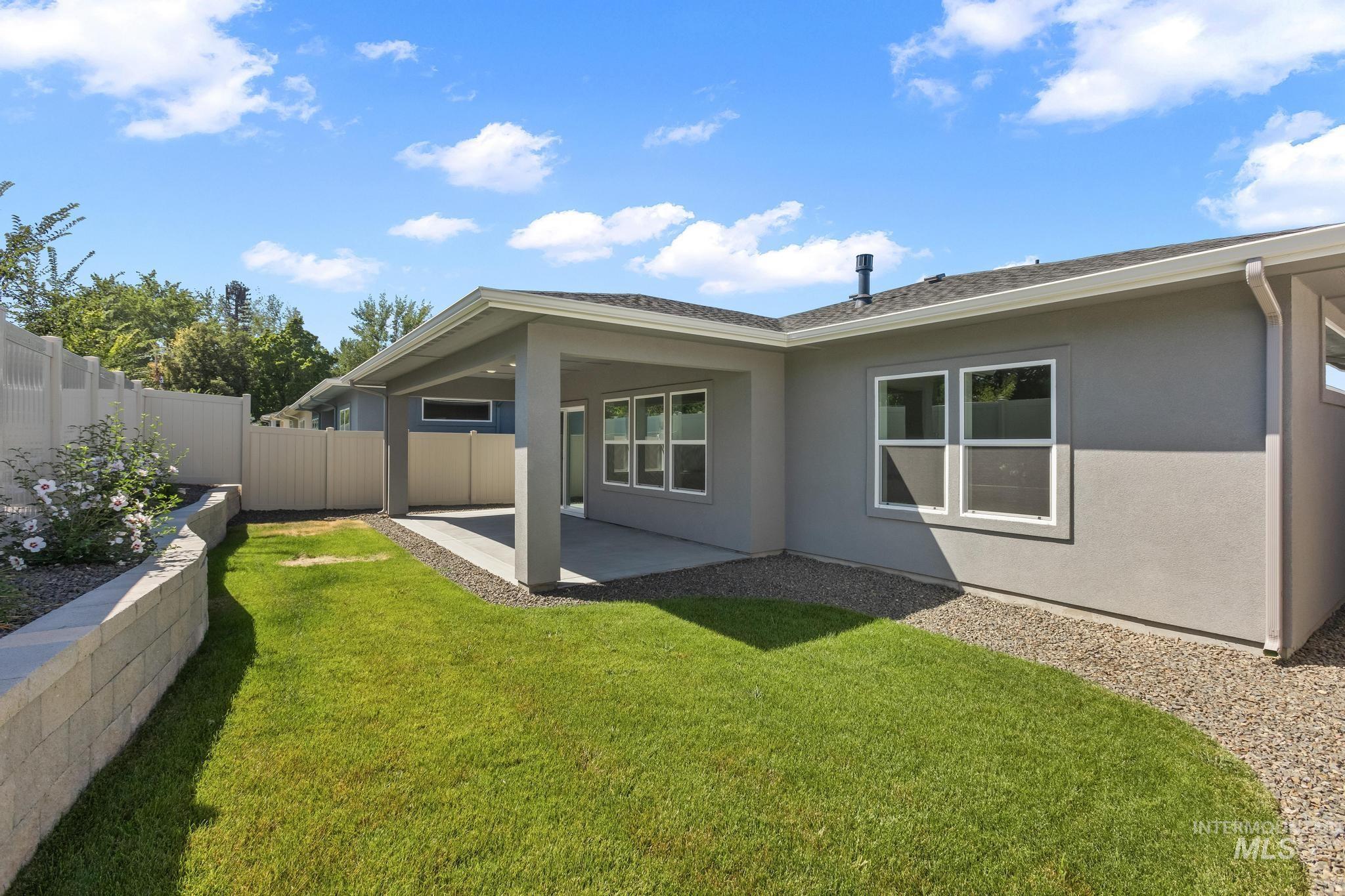 Rear view of house featuring stucco siding, covered patio, landscaped & fenced backyard with raised paver planter area