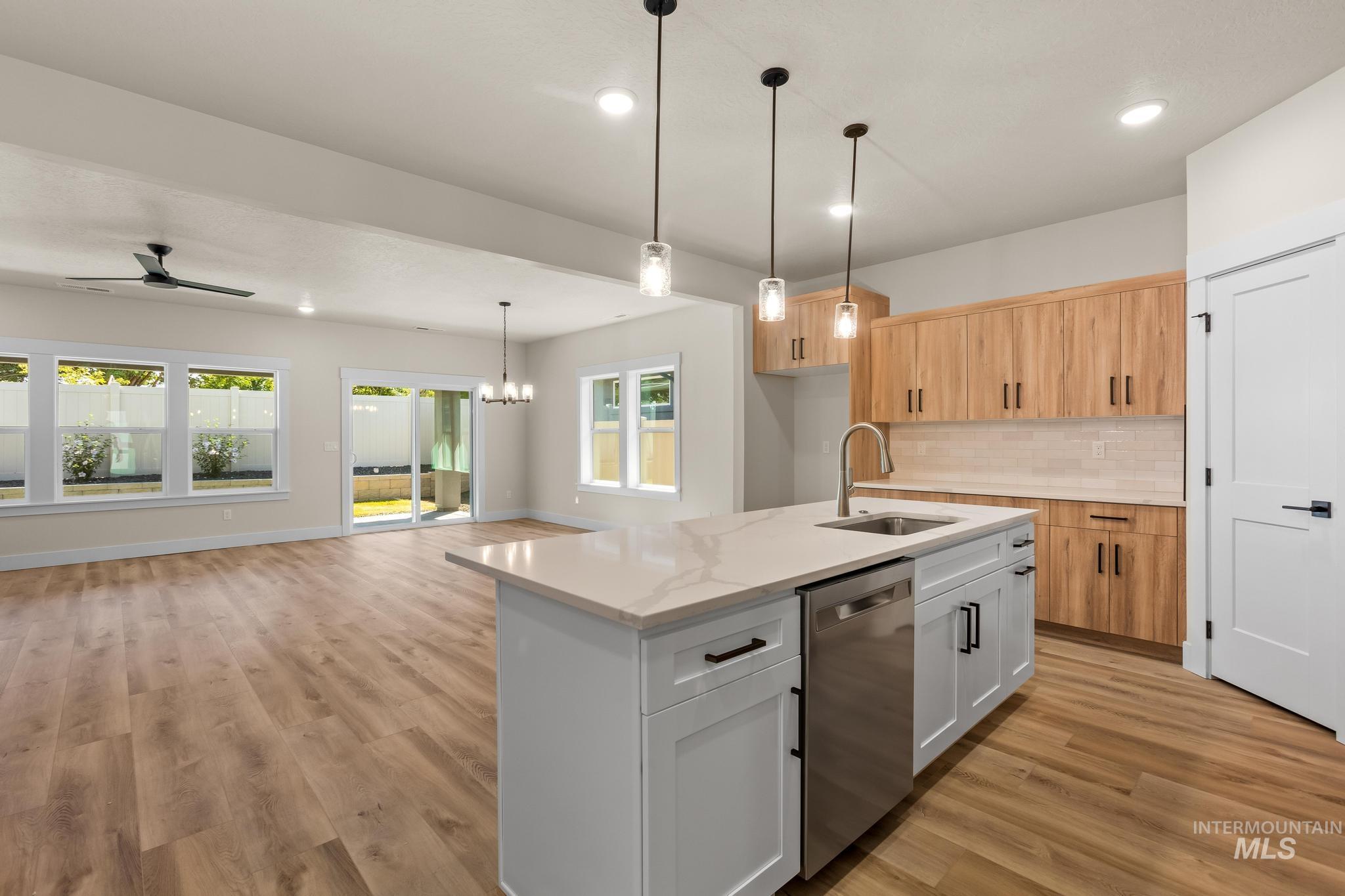 Kitchen with decorative backsplash, white cabinetry, dishwasher, open floor plan, and pendant lighting