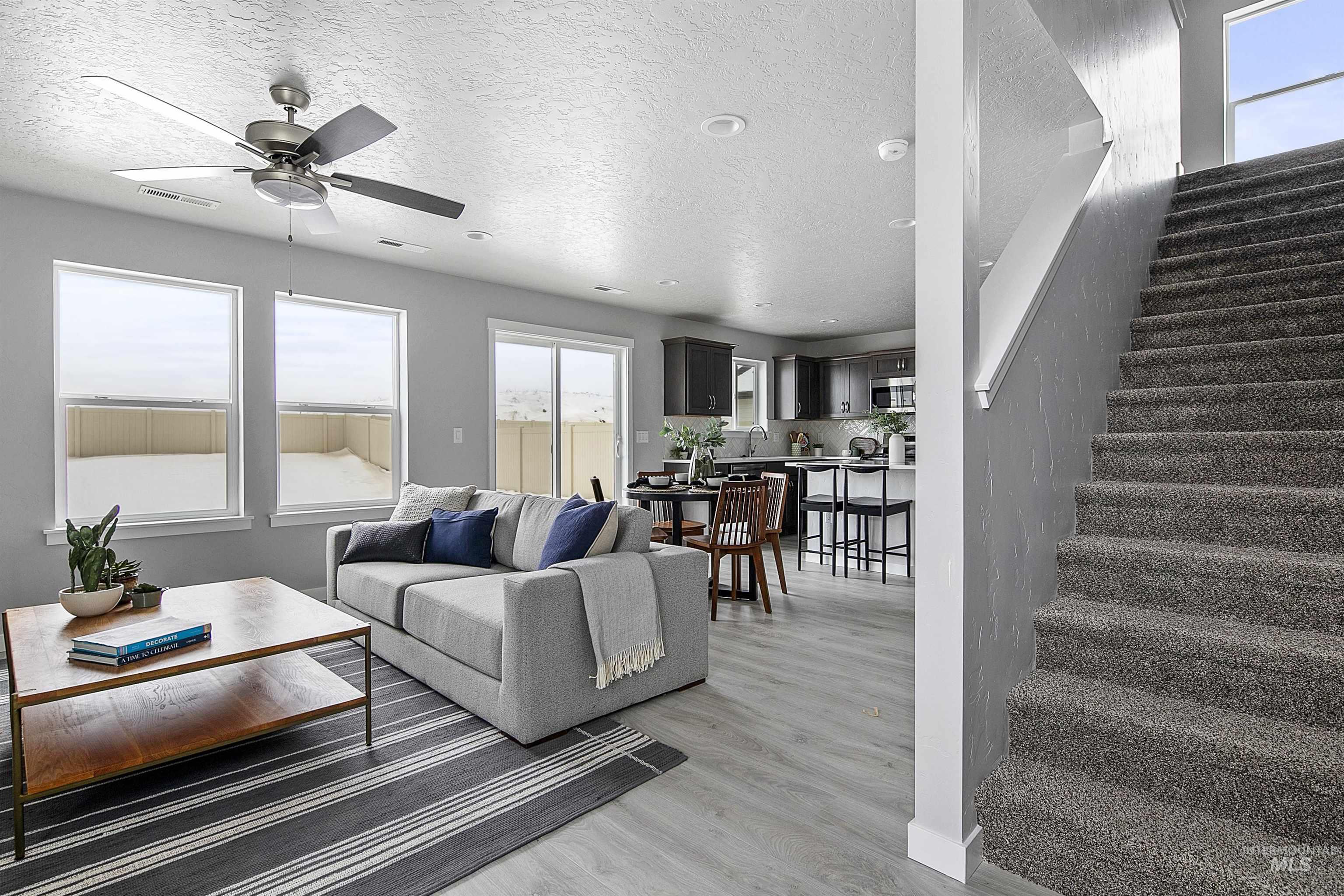 Living room with plenty of natural light, stairs, a textured ceiling, light wood finished floors, and a ceiling fan