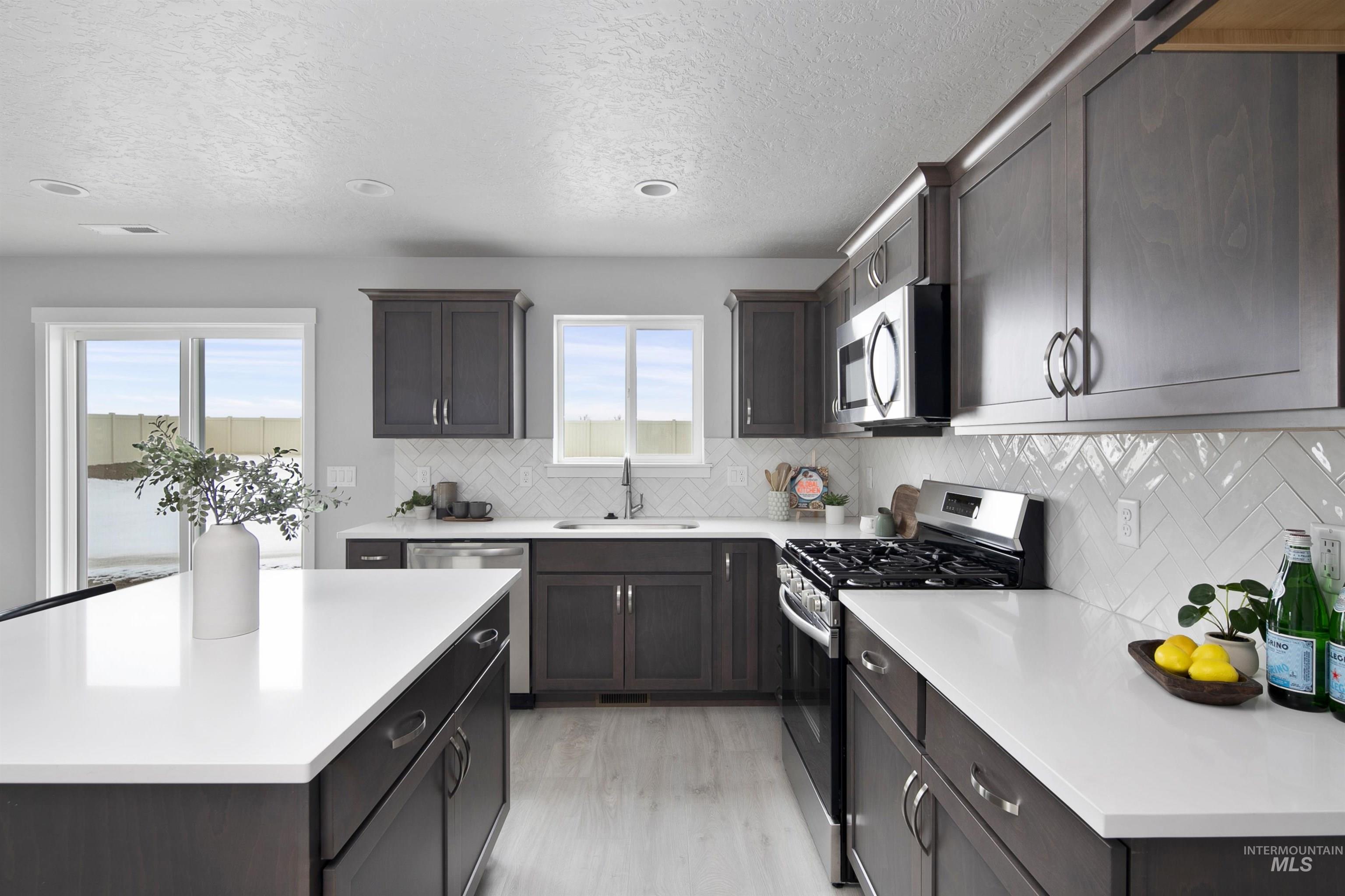 Kitchen with stainless steel appliances, decorative backsplash, a textured ceiling, light wood-type flooring, and a center island