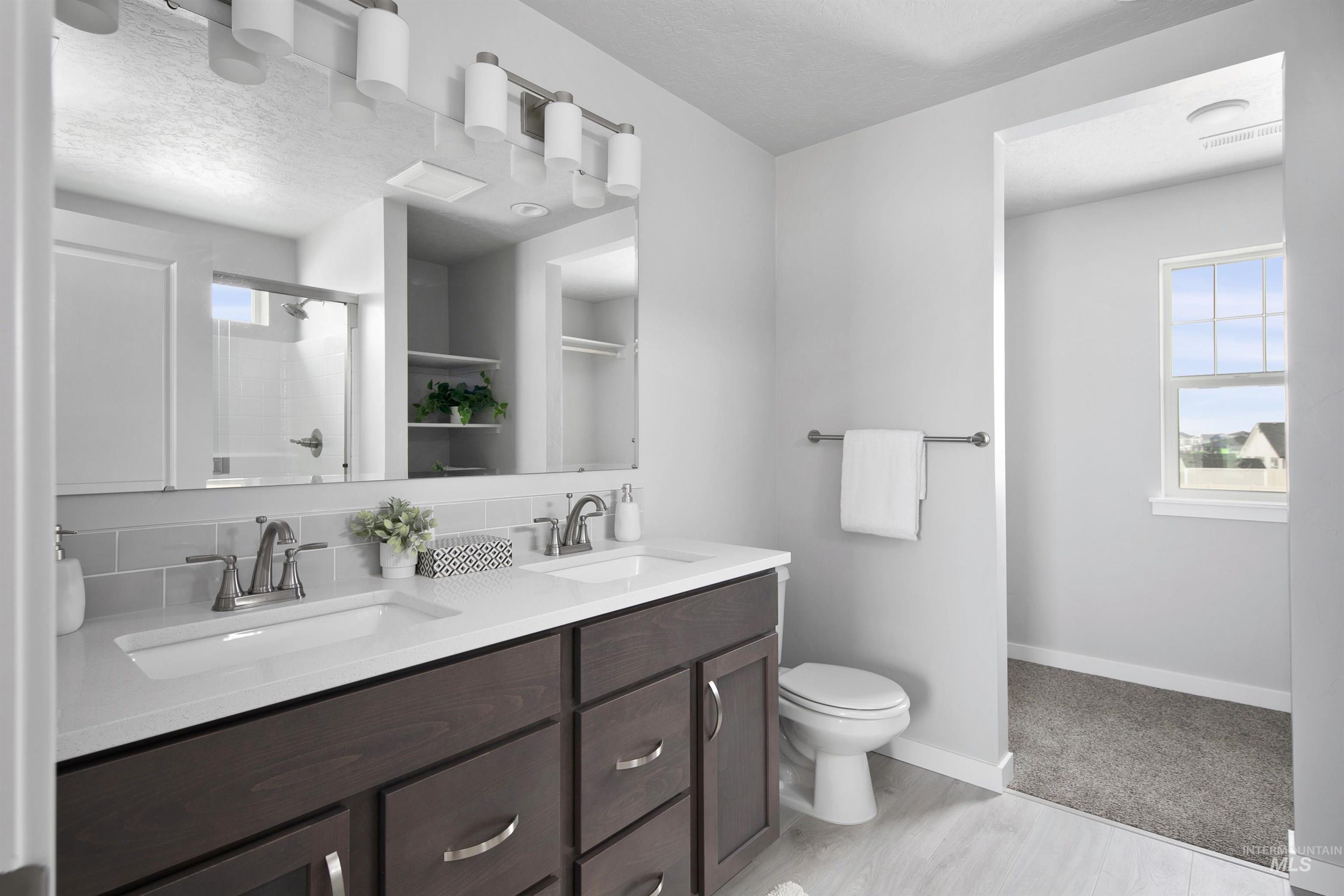 Bathroom featuring a stall shower, double vanity, a textured ceiling, and tasteful backsplash