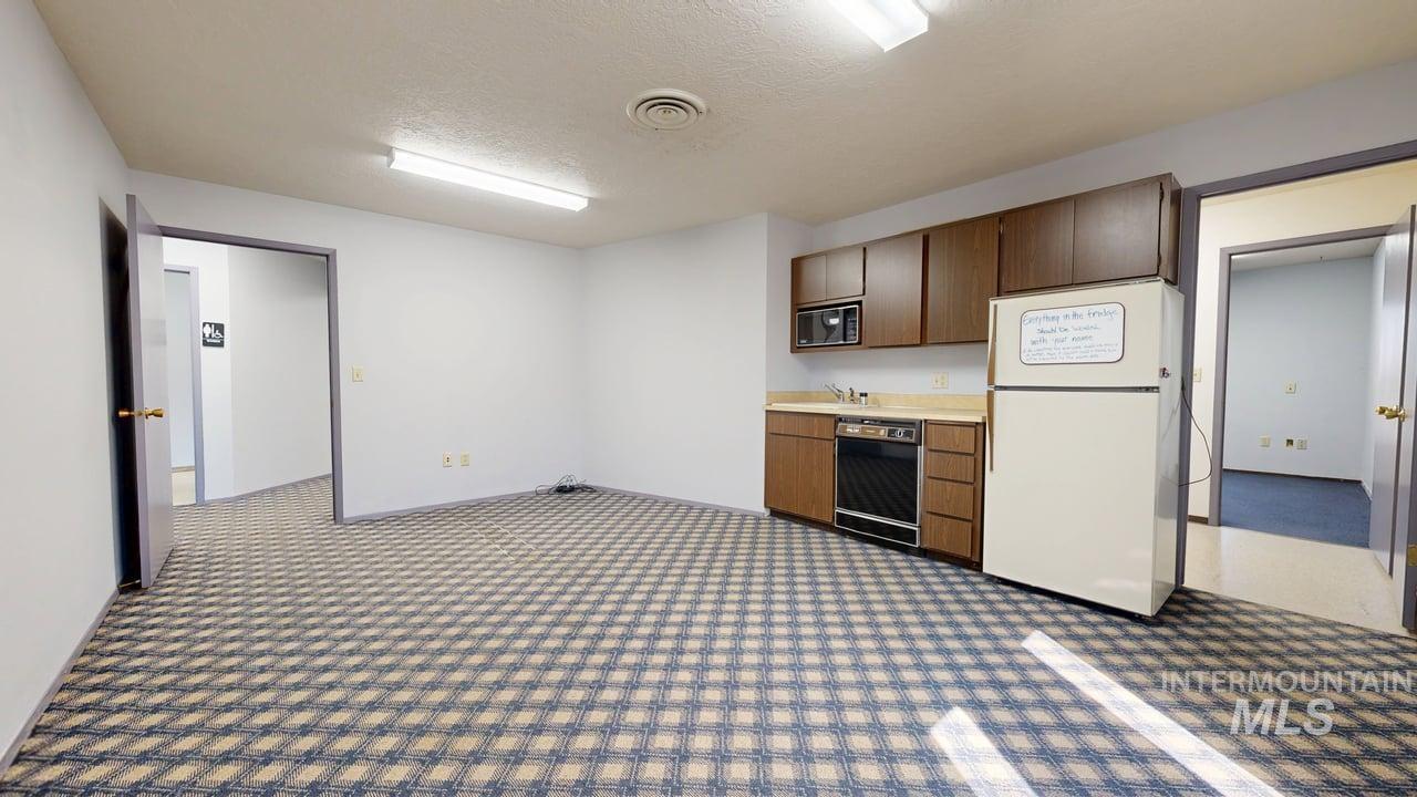 Kitchen with light countertops, black appliances, a textured ceiling, and dark carpet