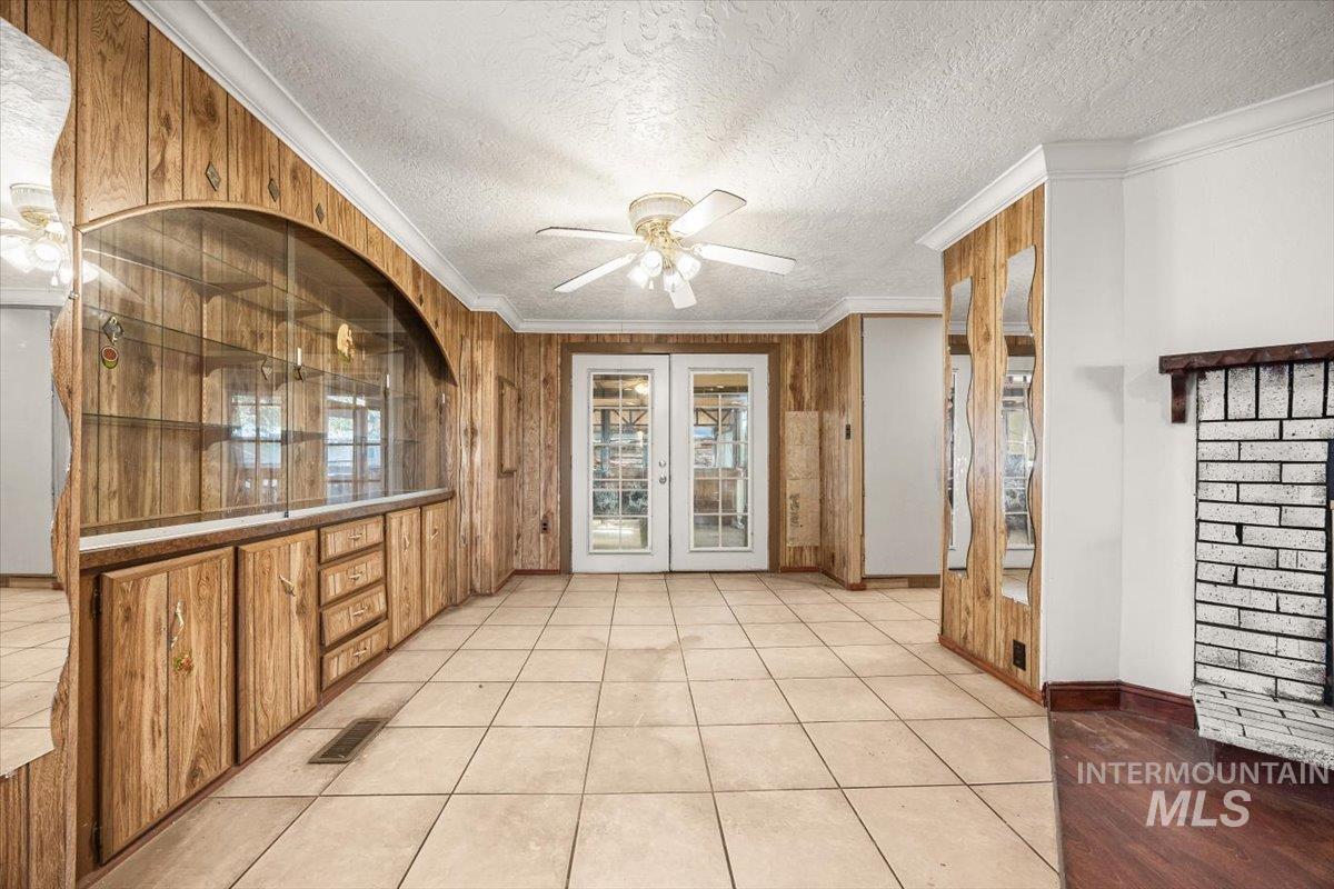 Unfurnished room featuring ceiling fan, crown molding, french doors, wooden walls, and a textured ceiling