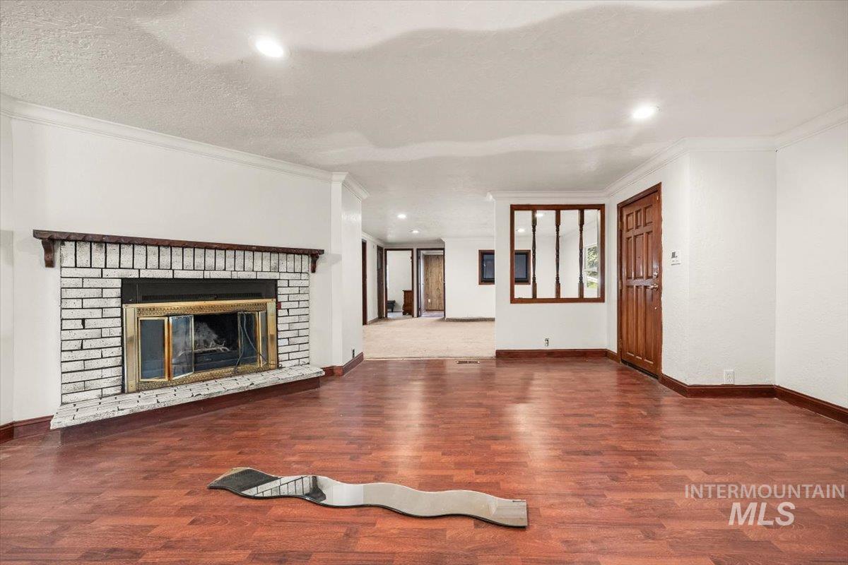 Unfurnished living room with a fireplace, dark wood-type flooring, ornamental molding, and a textured ceiling