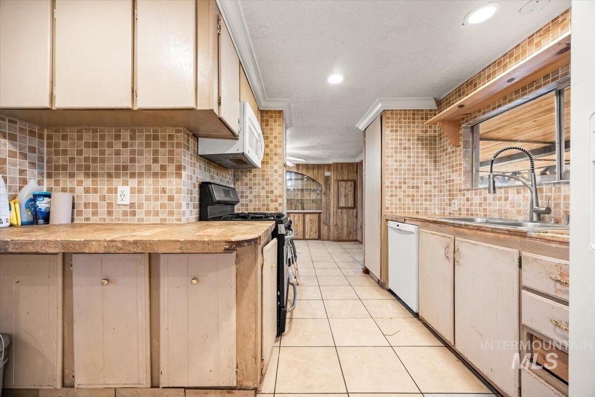 Kitchen with white appliances, backsplash, light tile patterned floors, ornamental molding, and a textured ceiling