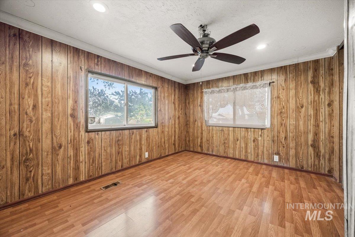 Empty room featuring crown molding, light wood-style flooring, wood walls, a textured ceiling, and a ceiling fan