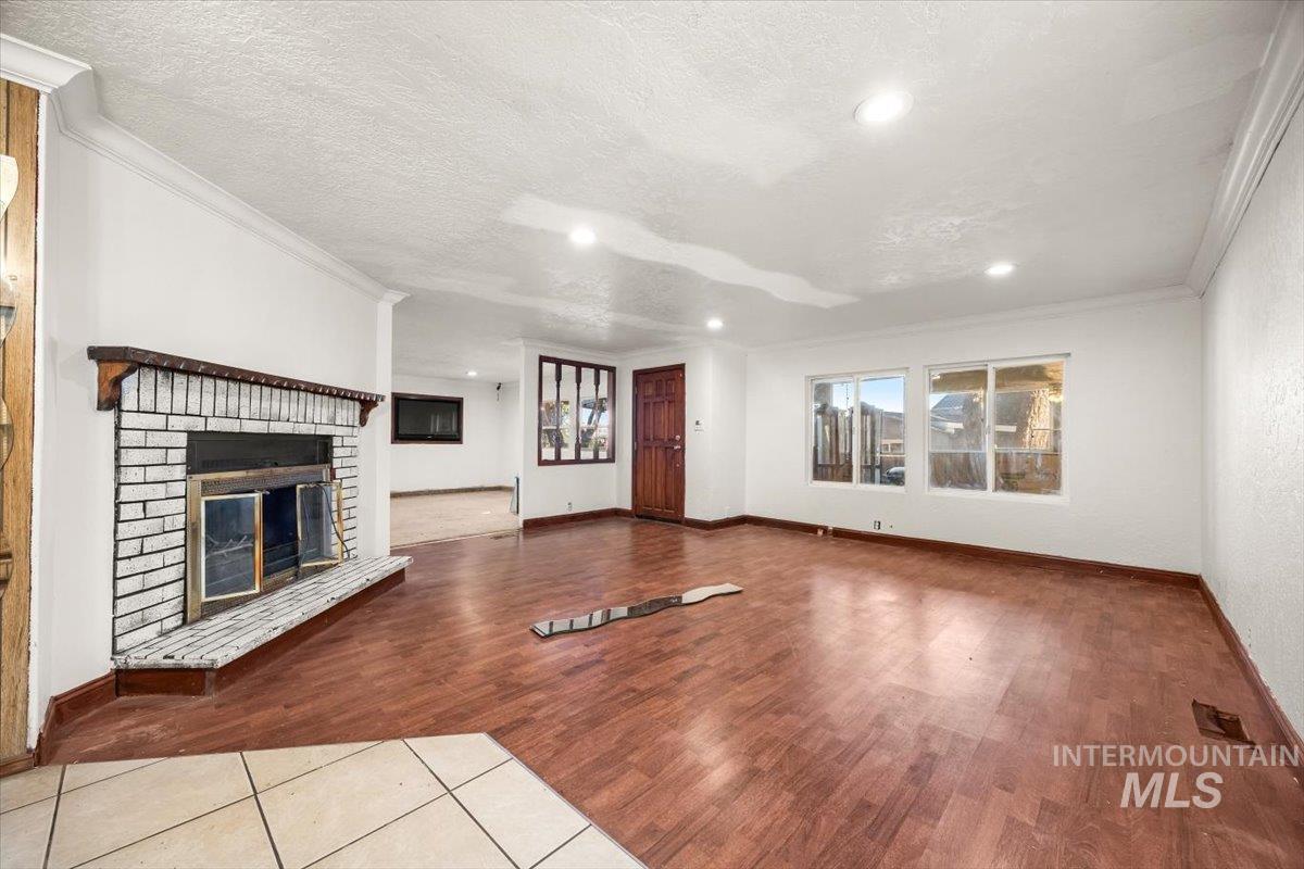 Unfurnished living room with crown molding, wood finished floors, a fireplace, a textured ceiling, and recessed lighting