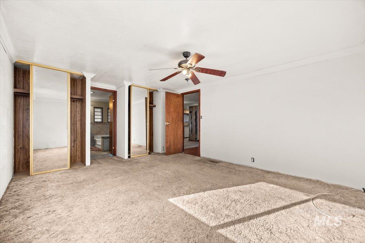 Unfurnished bedroom with carpet, crown molding, a ceiling fan, ensuite bathroom, and multiple closets