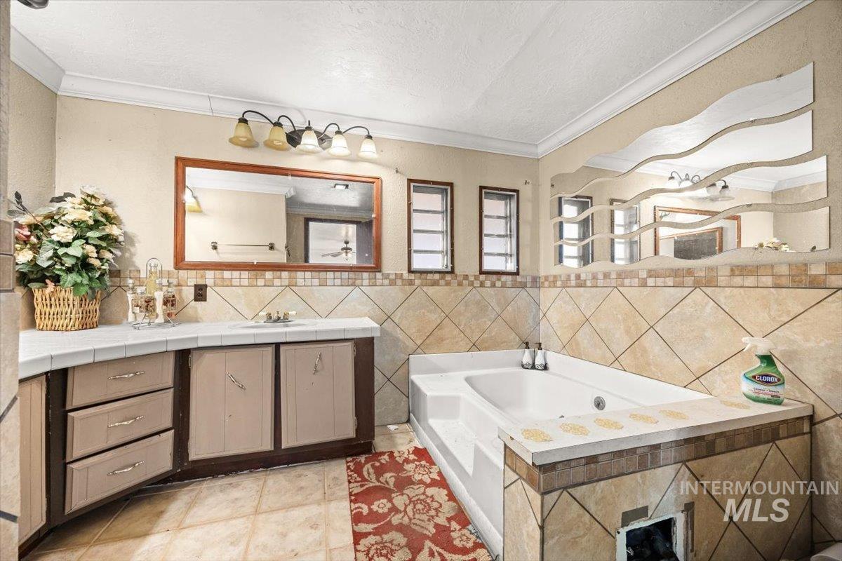 Bathroom featuring vanity, a jetted tub, crown molding, a textured ceiling, and tile walls