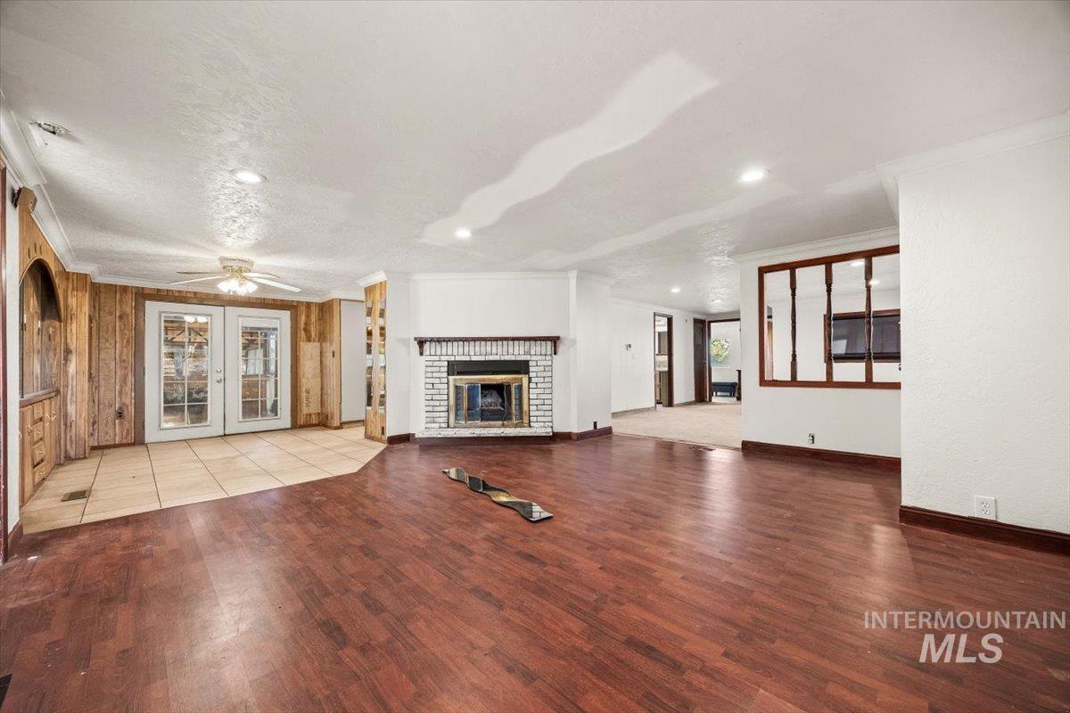 Unfurnished living room with ornamental molding, a brick fireplace, french doors, light wood-style flooring, and ceiling fan