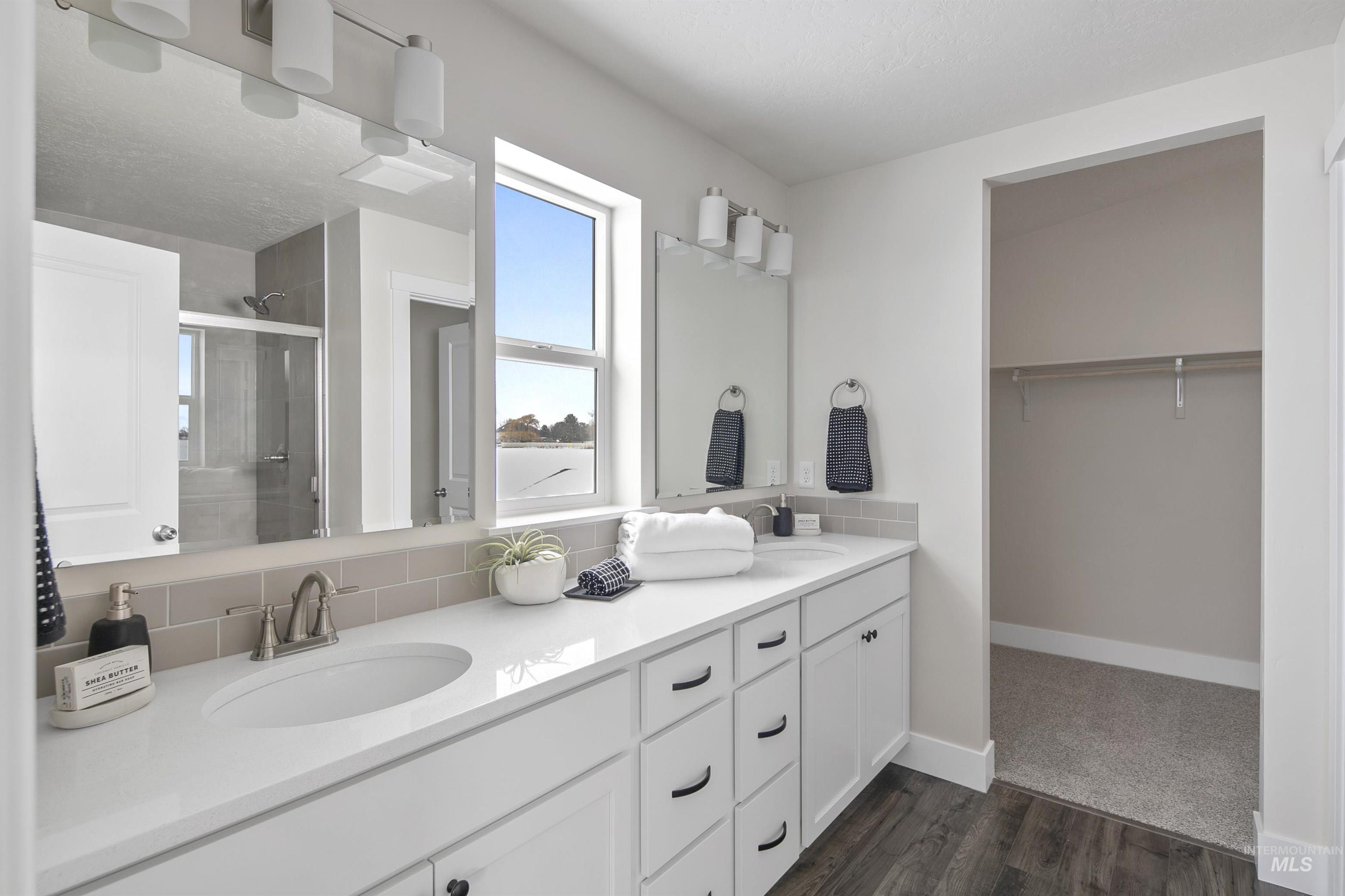 Bathroom with a stall shower, double vanity, dark wood finished floors, a spacious closet, and decorative backsplash