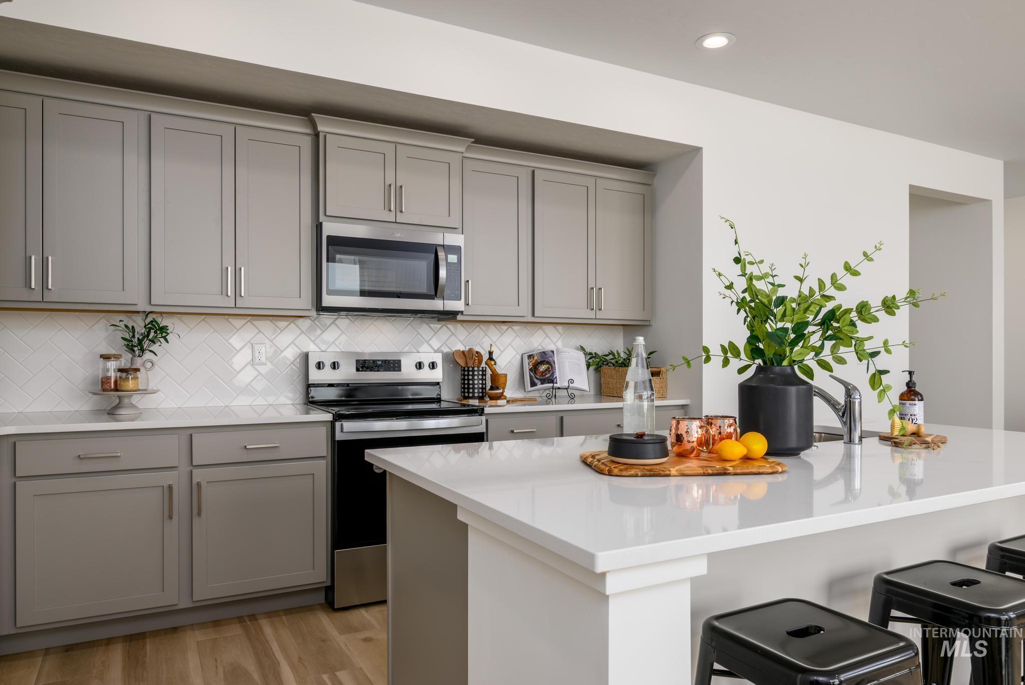 Kitchen with gray cabinetry, stainless steel appliances, light stone countertops, light wood-type flooring, and recessed lighting