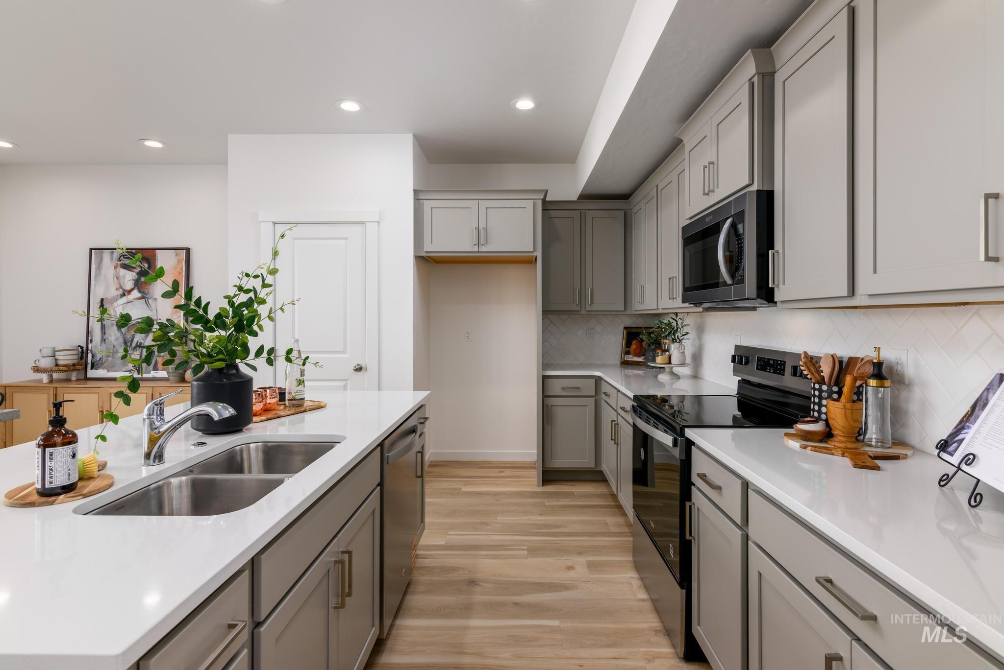 Kitchen featuring appliances with stainless steel finishes, gray cabinetry, recessed lighting, and an island with sink