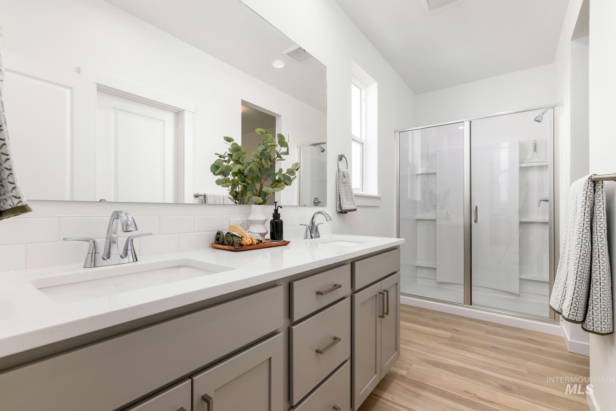 Bathroom with a stall shower, double vanity, light wood-type flooring, and tasteful backsplash