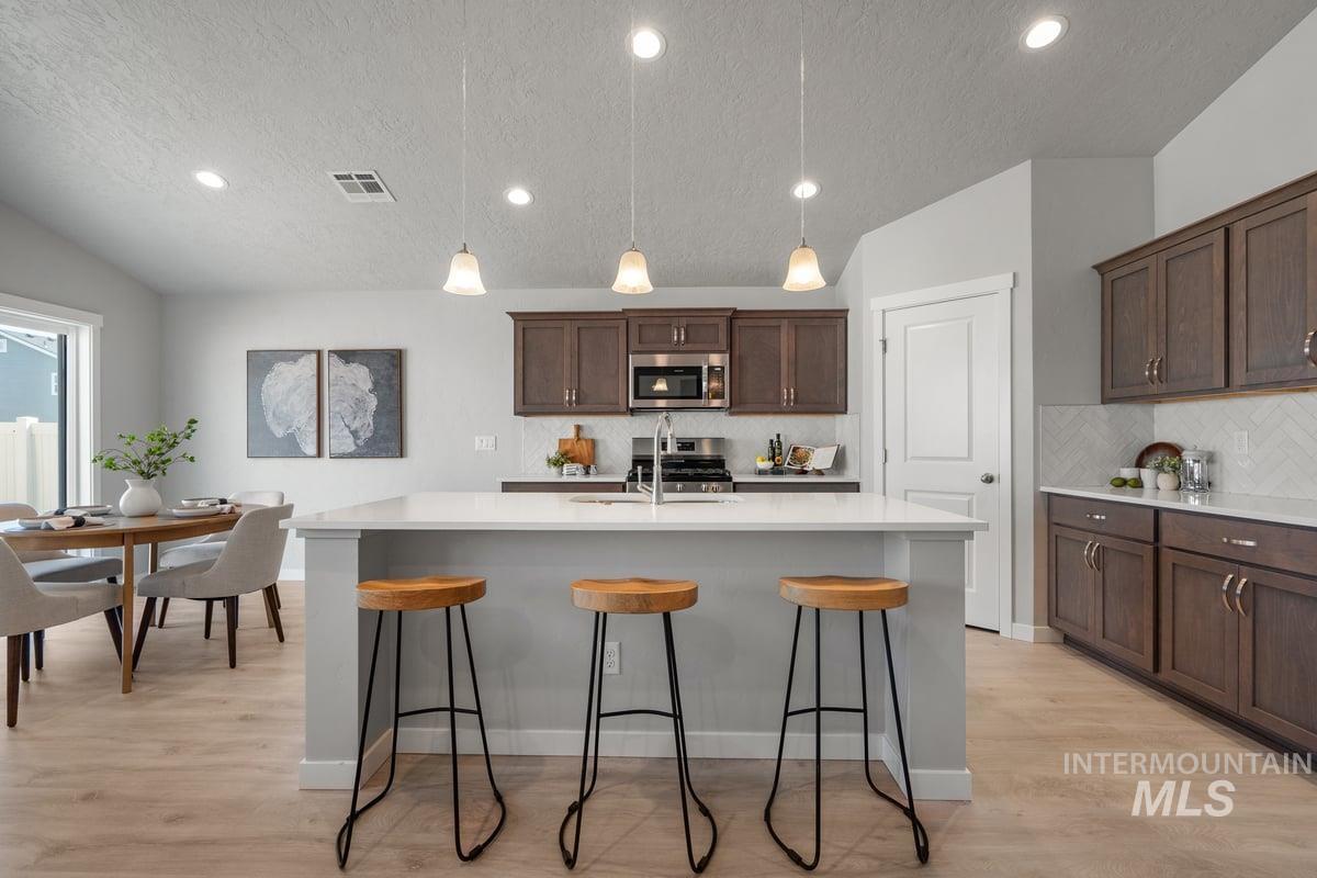 Kitchen with a textured ceiling, hanging light fixtures, dark brown cabinets, light wood-style flooring, and recessed lighting