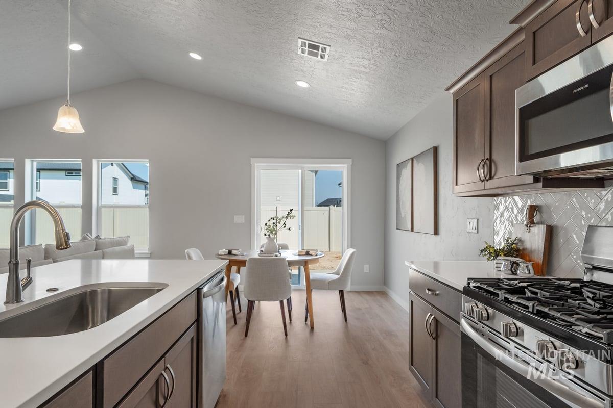 Kitchen with stainless steel appliances, dark brown cabinetry, light wood finished floors, plenty of natural light, and lofted ceiling