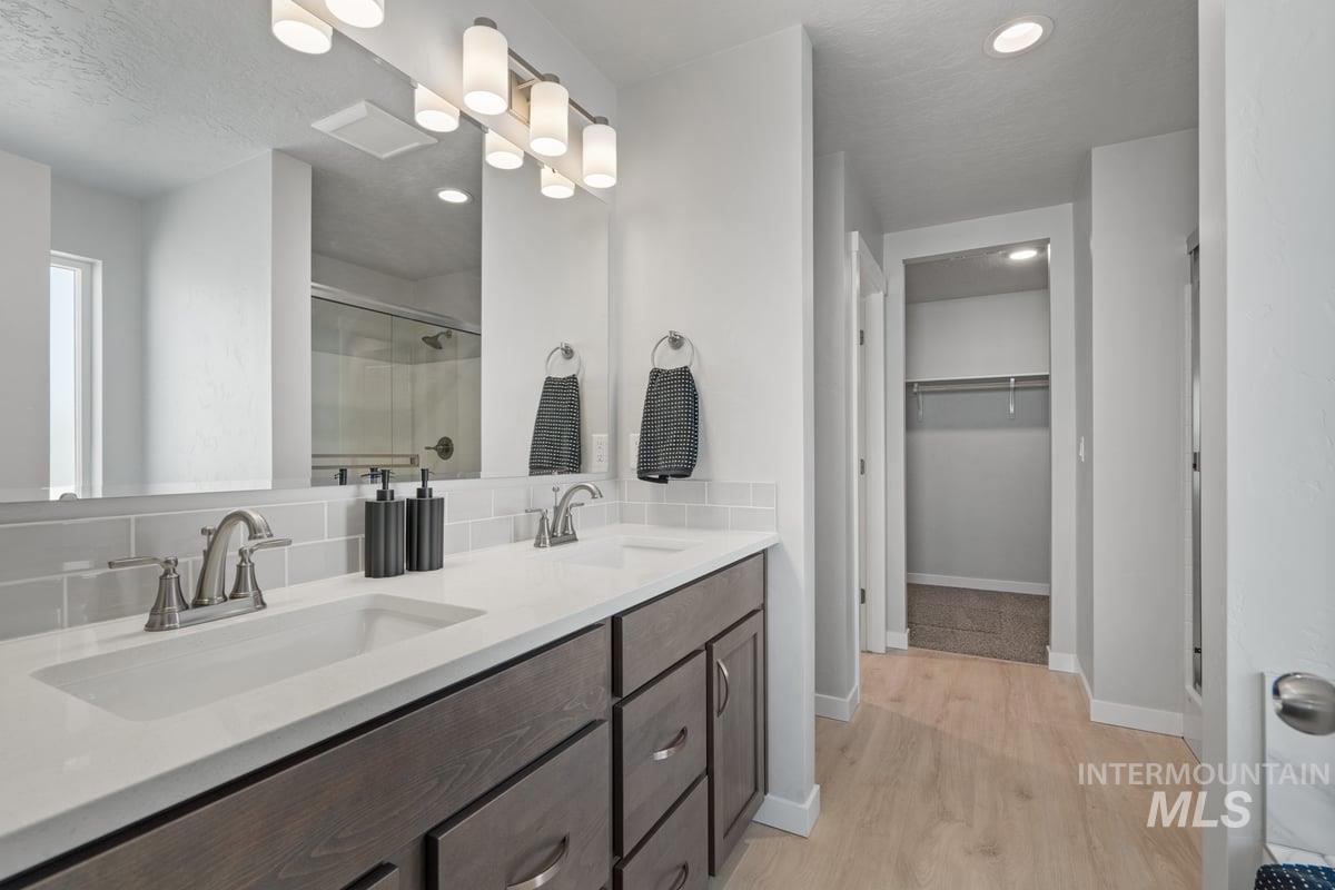 Full bath featuring a shower stall, light wood-style flooring, double vanity, a spacious closet, and recessed lighting