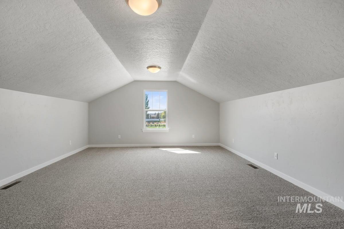 Bonus room featuring carpet flooring, vaulted ceiling, and a textured ceiling
