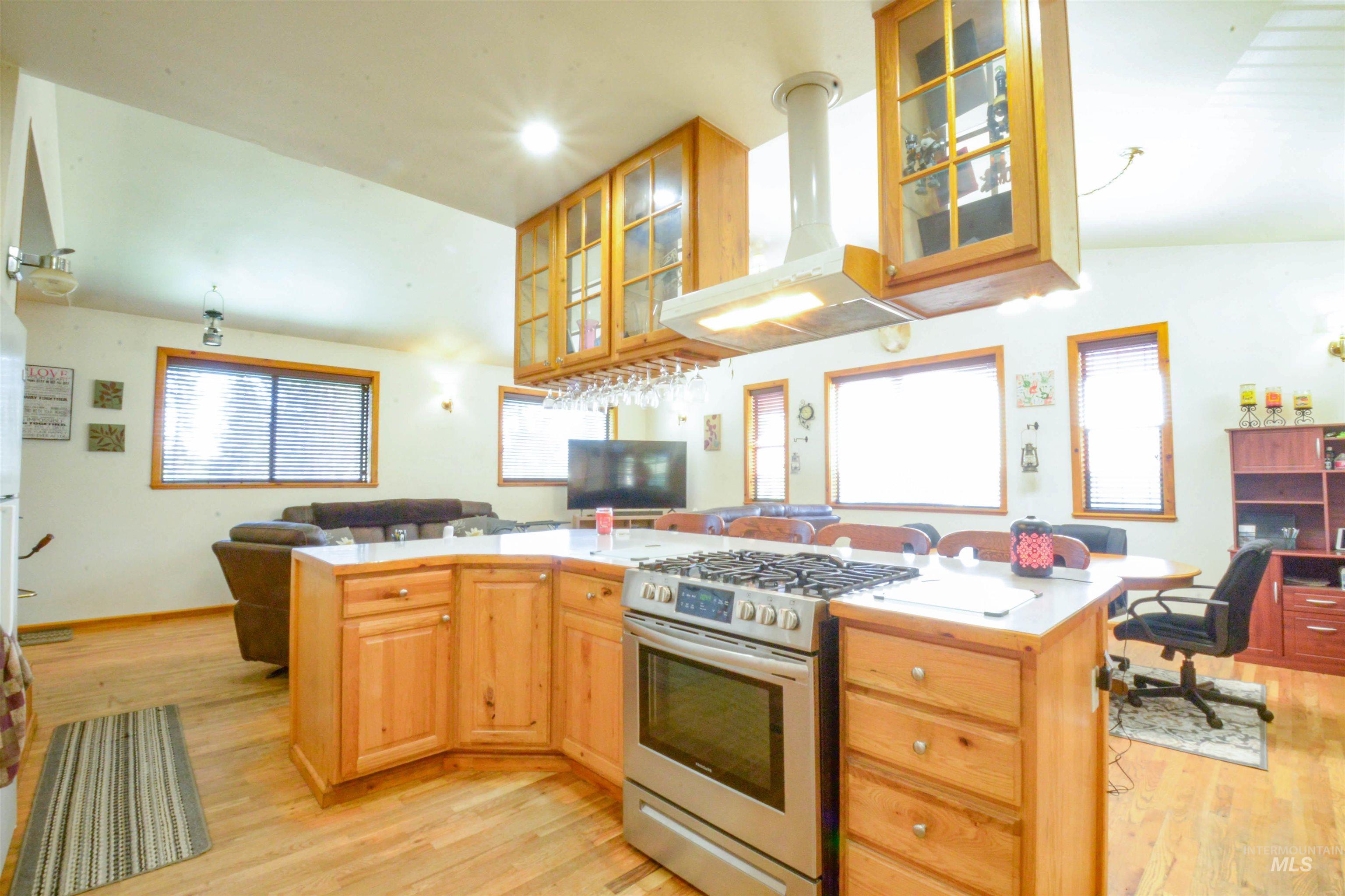 Kitchen with open floor plan, gas range, exhaust hood, glass insert cabinets, and light countertops