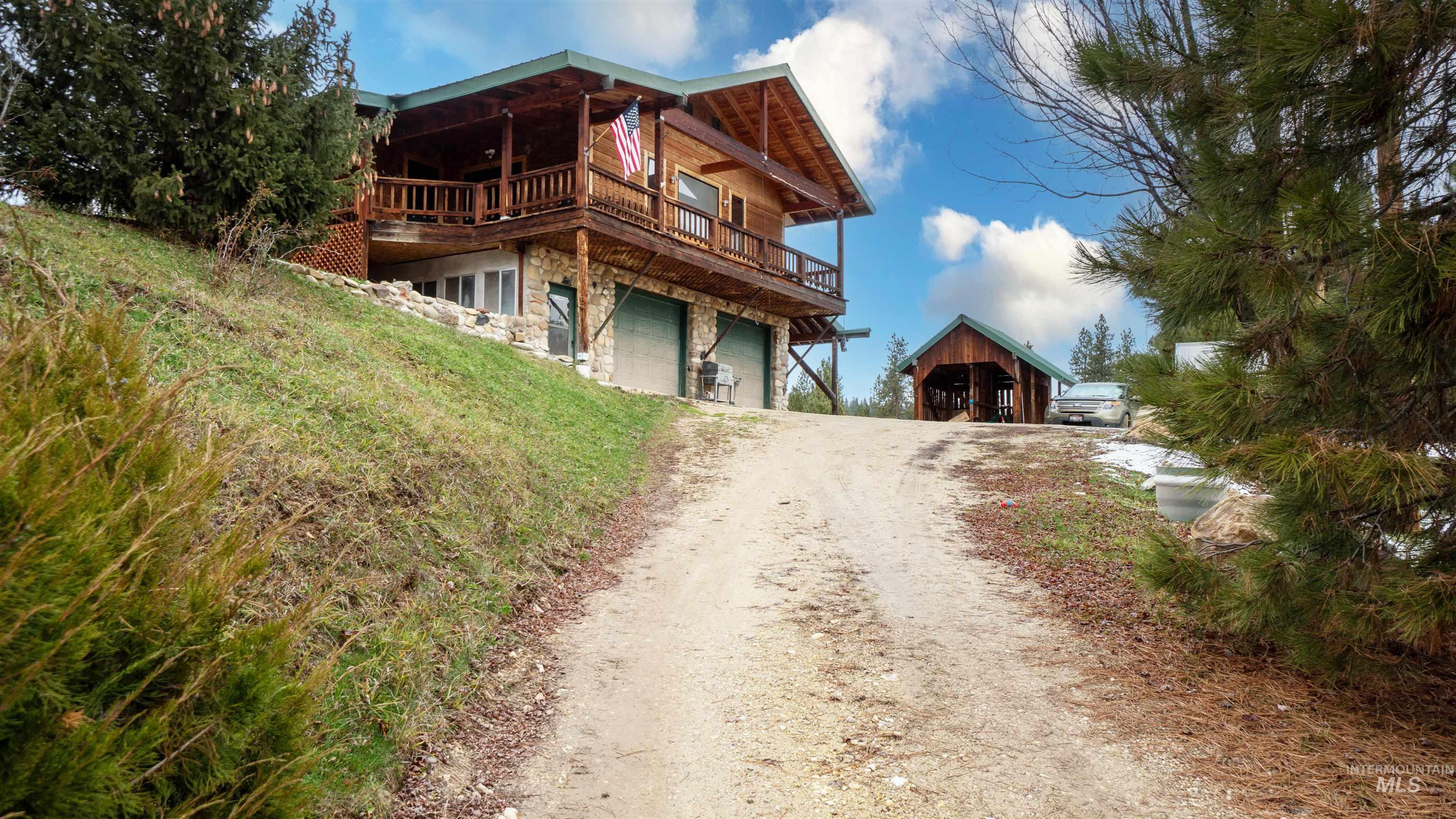 Rear view of property with a deck, dirt driveway, stone siding, and an attached garage