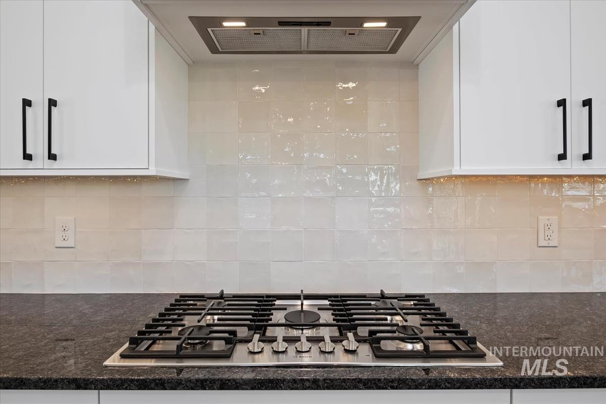 Kitchen featuring exhaust hood, stainless steel gas cooktop, dark stone counters, and white cabinetry