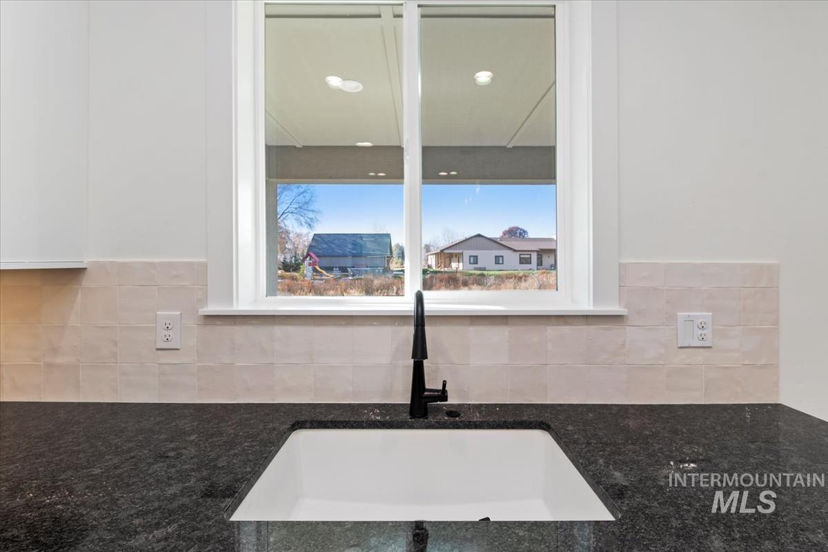 Kitchen view of dark stone counters, white cabinets, and tasteful backsplash