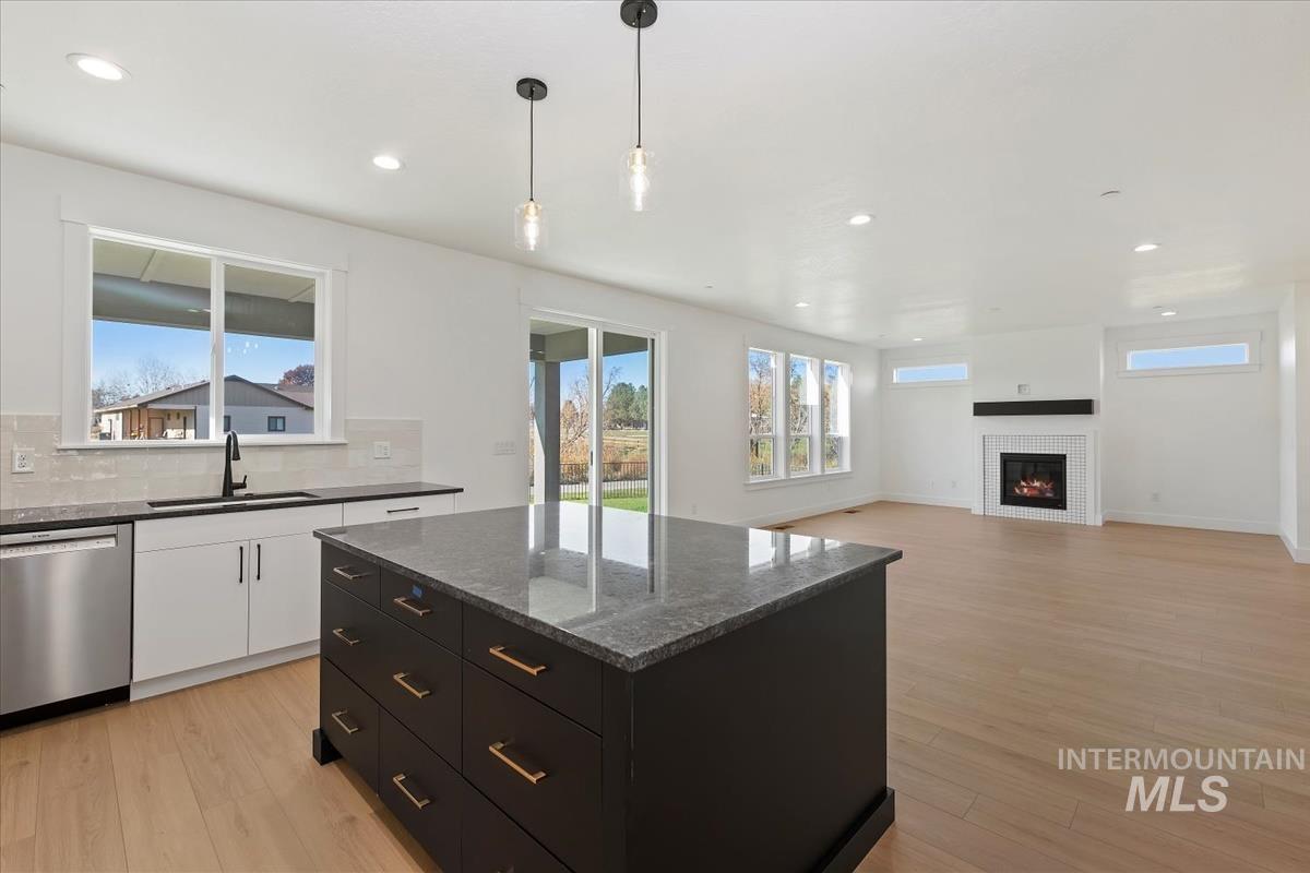 Kitchen with dark cabinets, pendant lighting, dishwasher, tasteful backsplash, and dark stone countertops