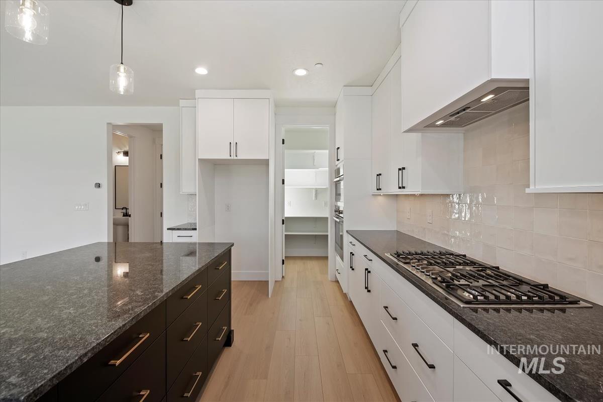 Kitchen with dark stone countertops, white cabinets, pendant lighting, light wood finished floors, and stainless steel gas stovetop
