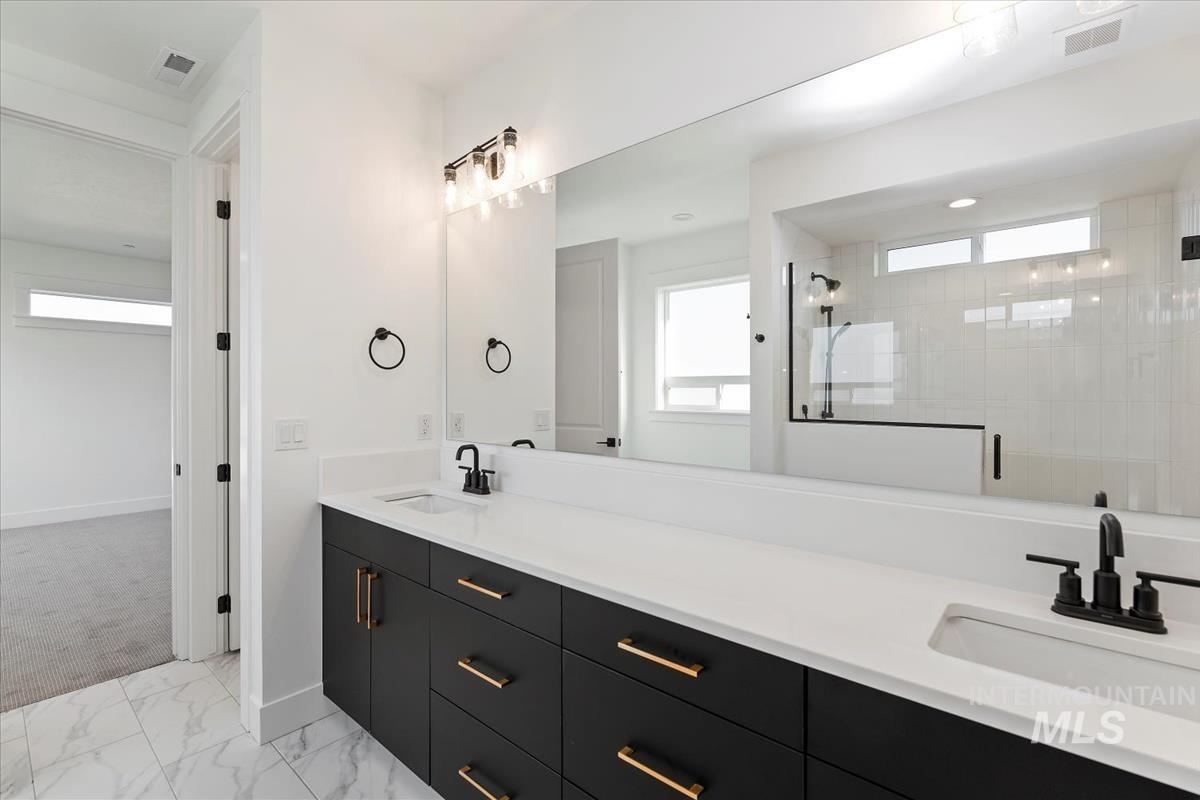 Full bath featuring double vanity, a stall shower, and light marble finish floors