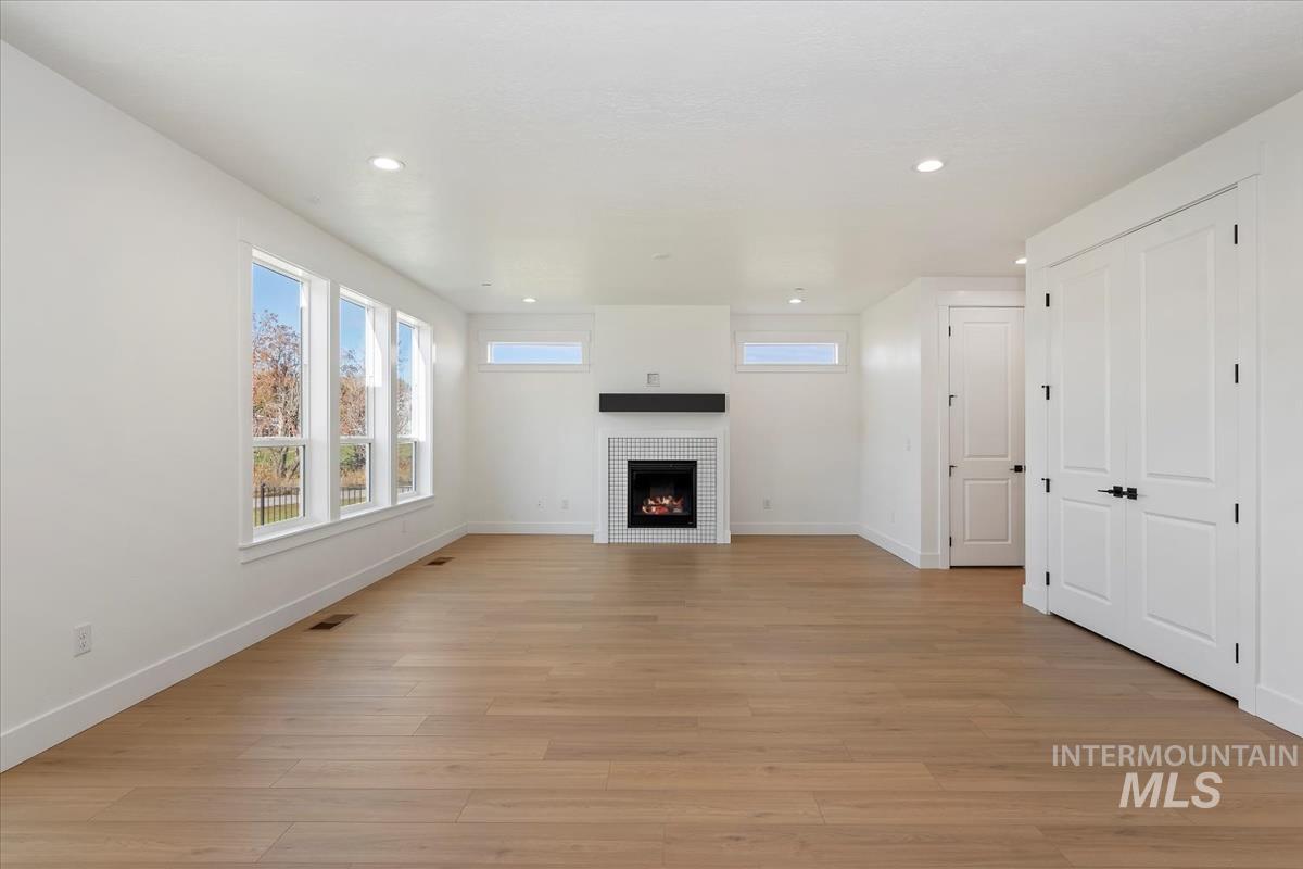 Unfurnished living room with light wood-style flooring, recessed lighting, and a warm lit fireplace