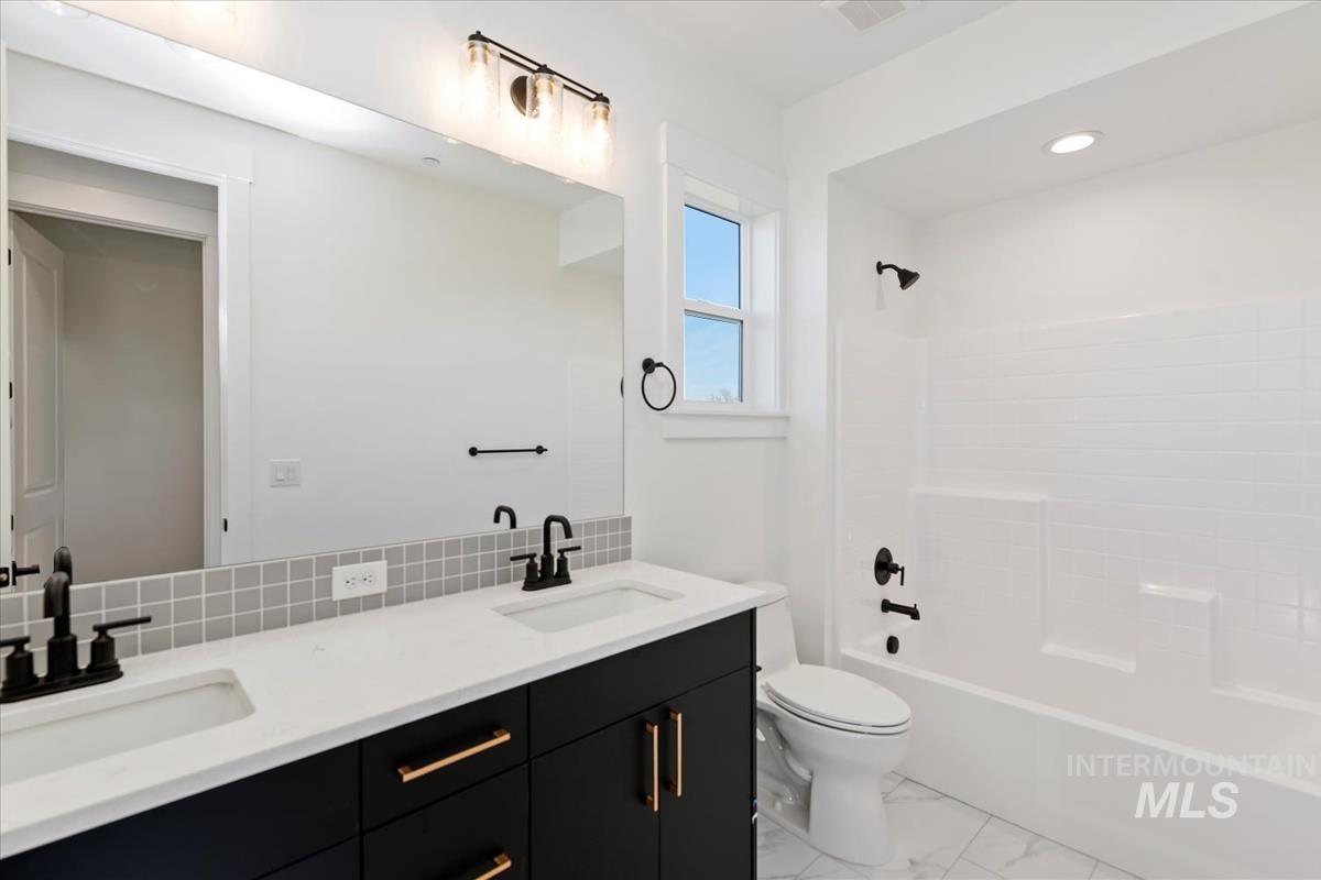 Full bathroom with double vanity, shower / bathtub combination, light marble finish floors, backsplash, and recessed lighting