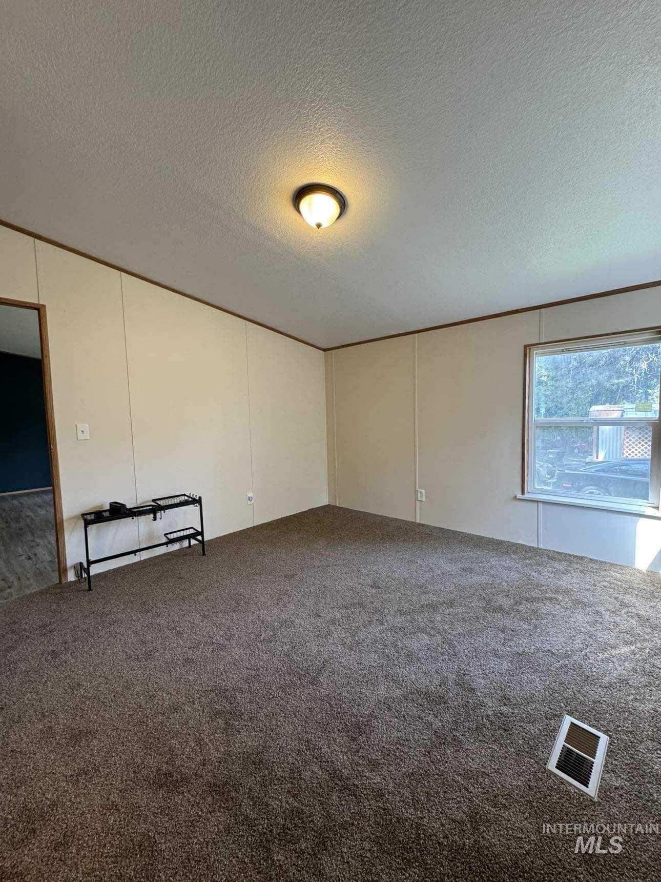 Carpeted empty room featuring a textured ceiling and a decorative wall