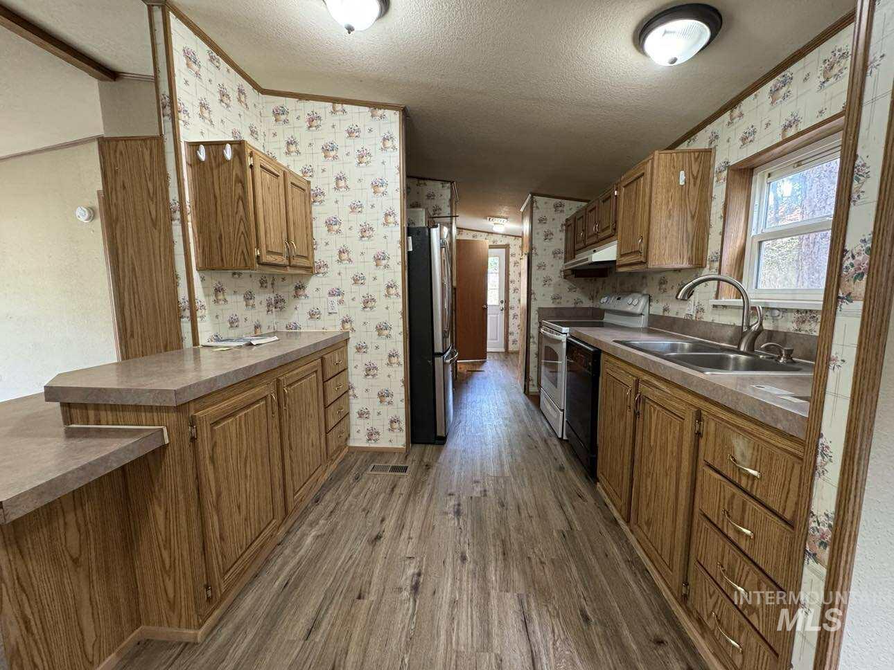 Kitchen with a textured ceiling, dark wood finished floors, electric range, freestanding refrigerator, and wallpapered walls