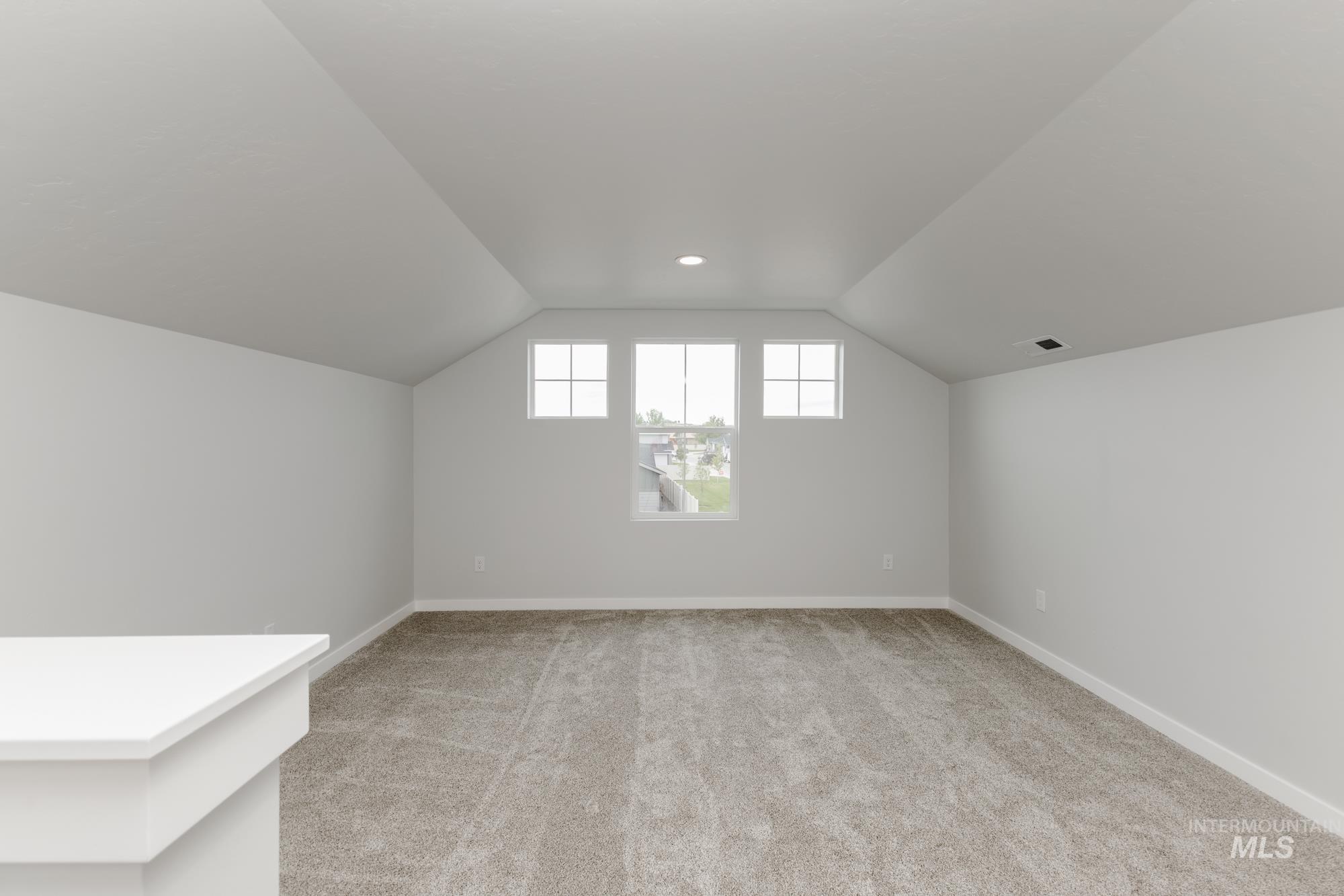 Bonus room with lofted ceiling and light colored carpet
