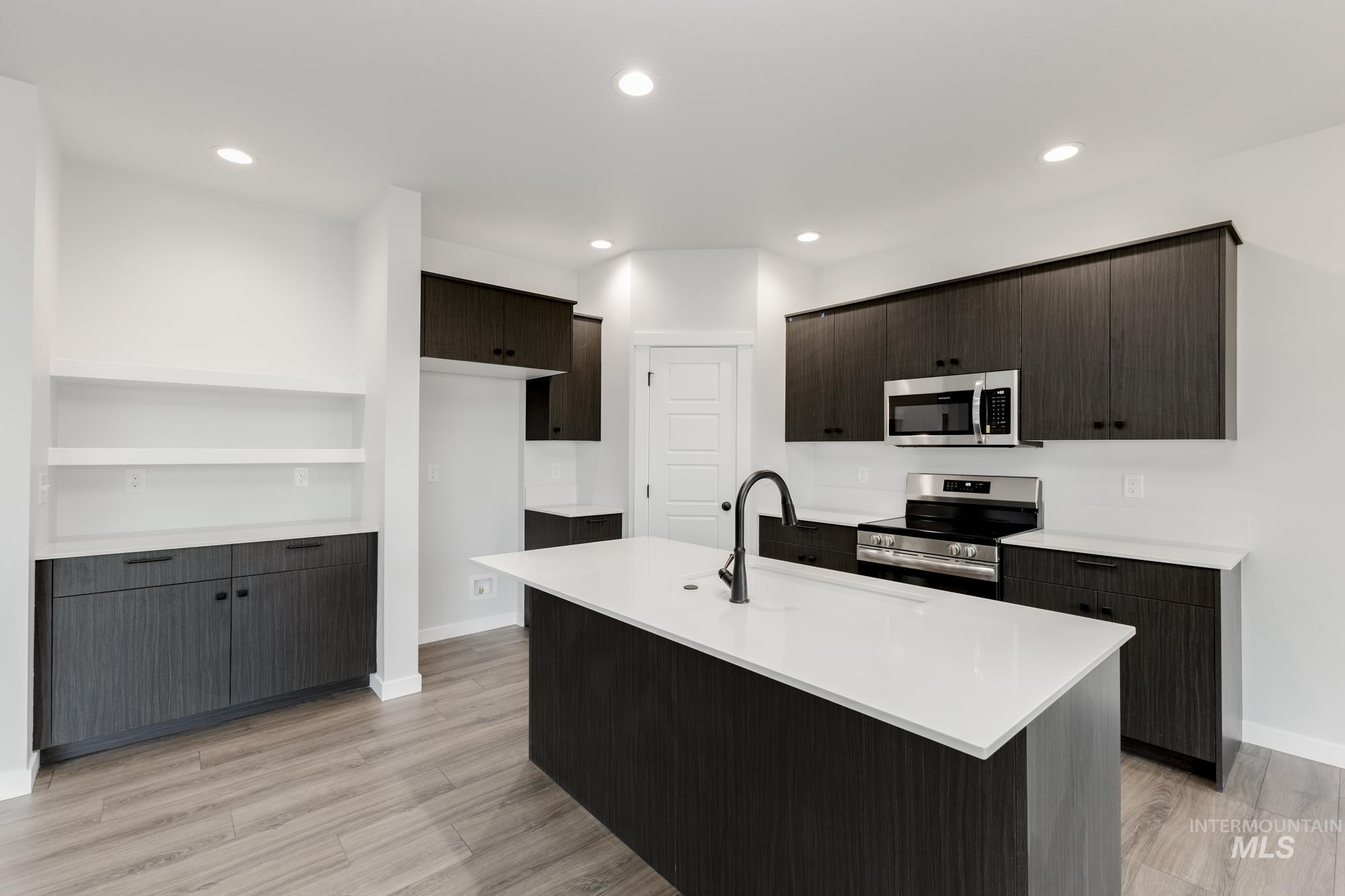 Kitchen featuring appliances with stainless steel finishes, light wood-style flooring, light countertops, recessed lighting, and an island with sink
