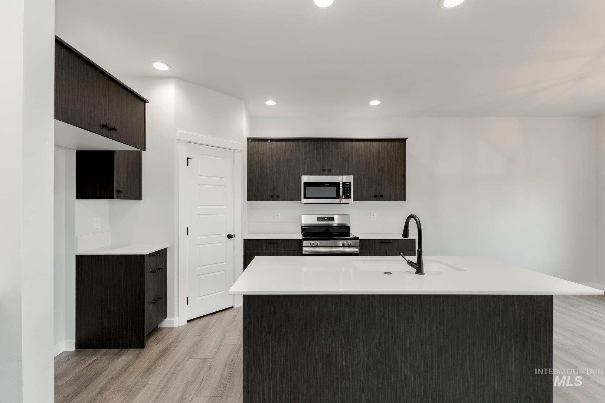 Kitchen with stainless steel appliances, light wood-style floors, light countertops, recessed lighting, and a center island with sink