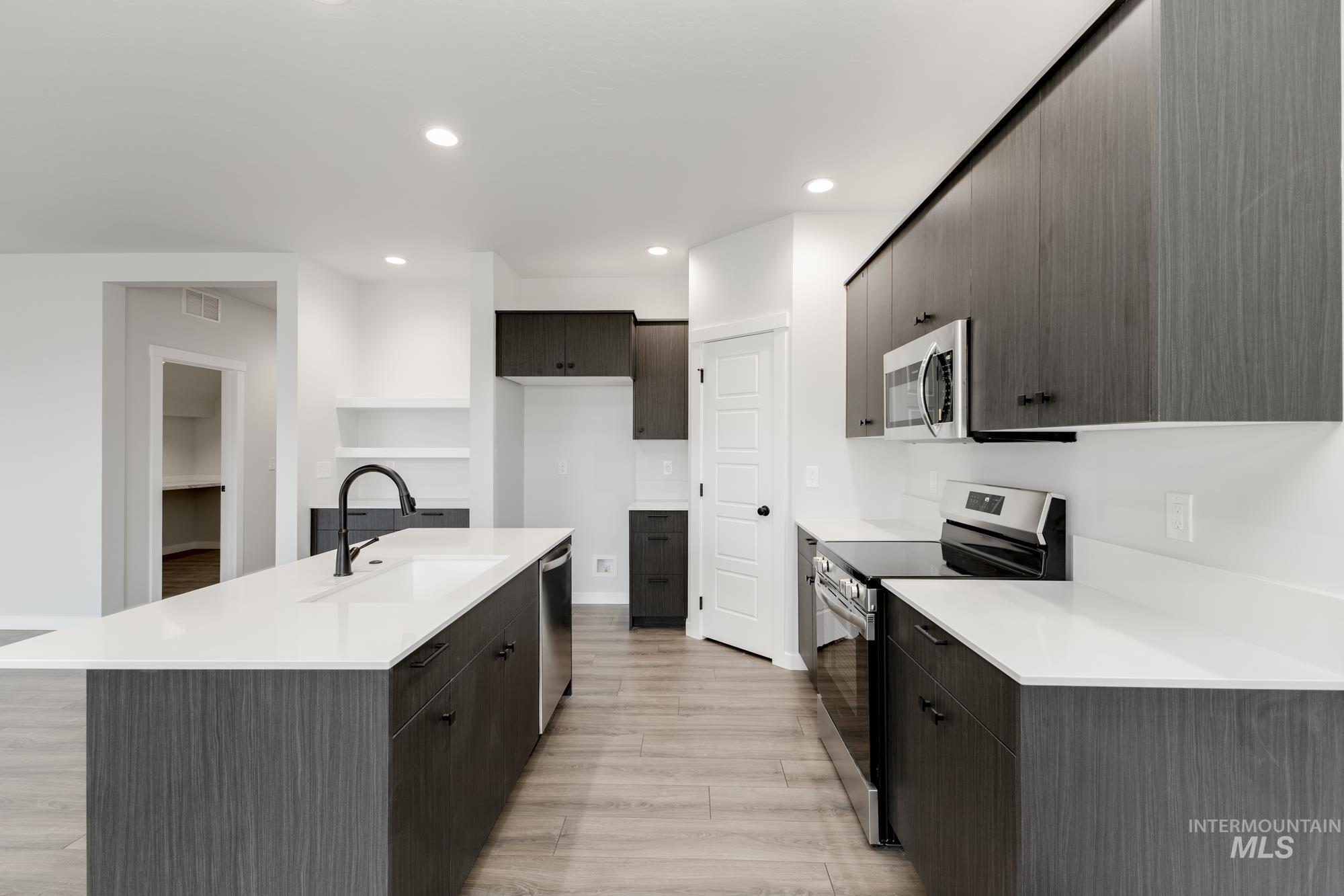Kitchen featuring appliances with stainless steel finishes, light wood-style flooring, a kitchen island with sink, light countertops, and recessed lighting