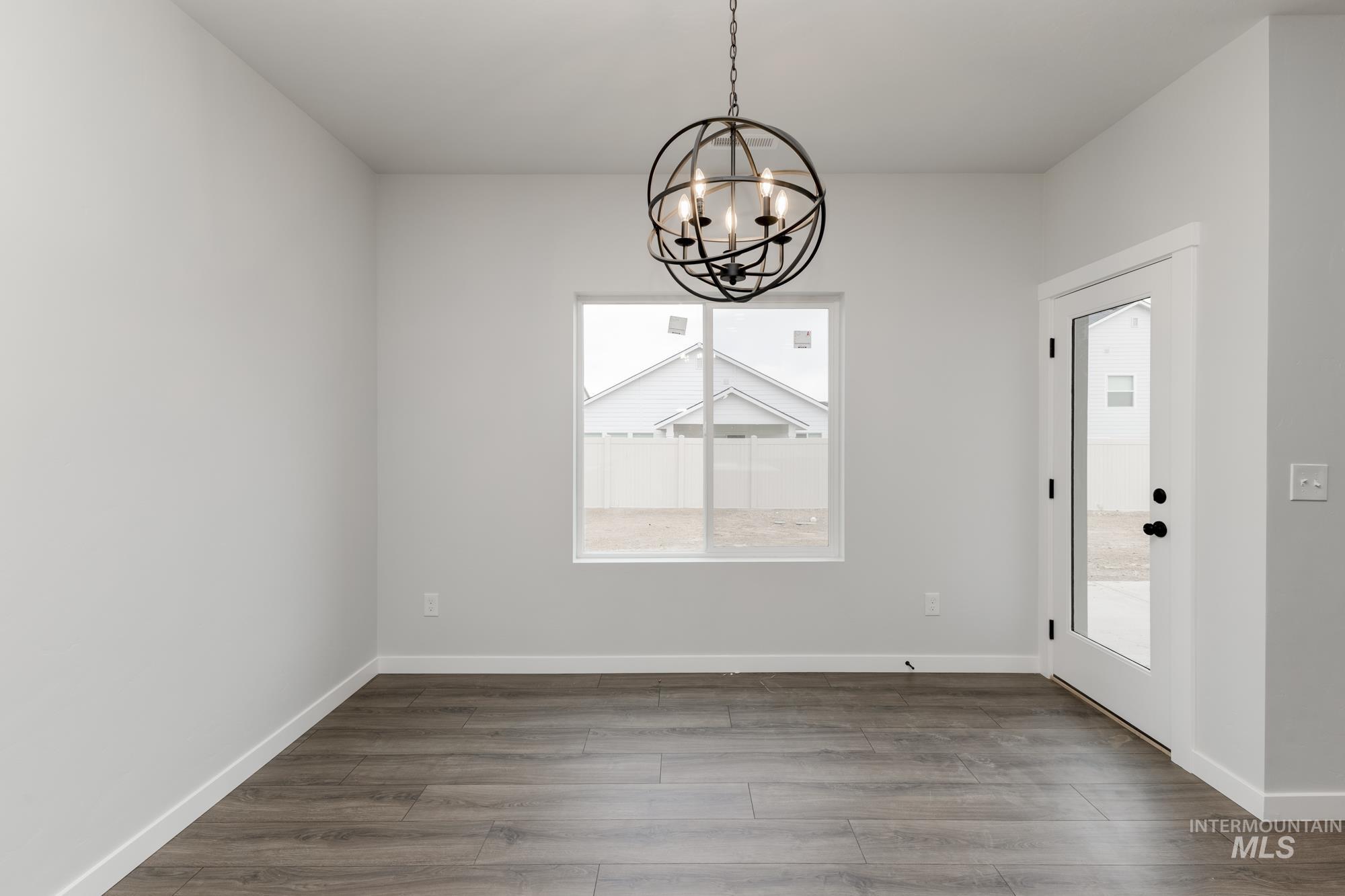 Unfurnished dining area with a chandelier, healthy amount of natural light, and dark wood-style flooring