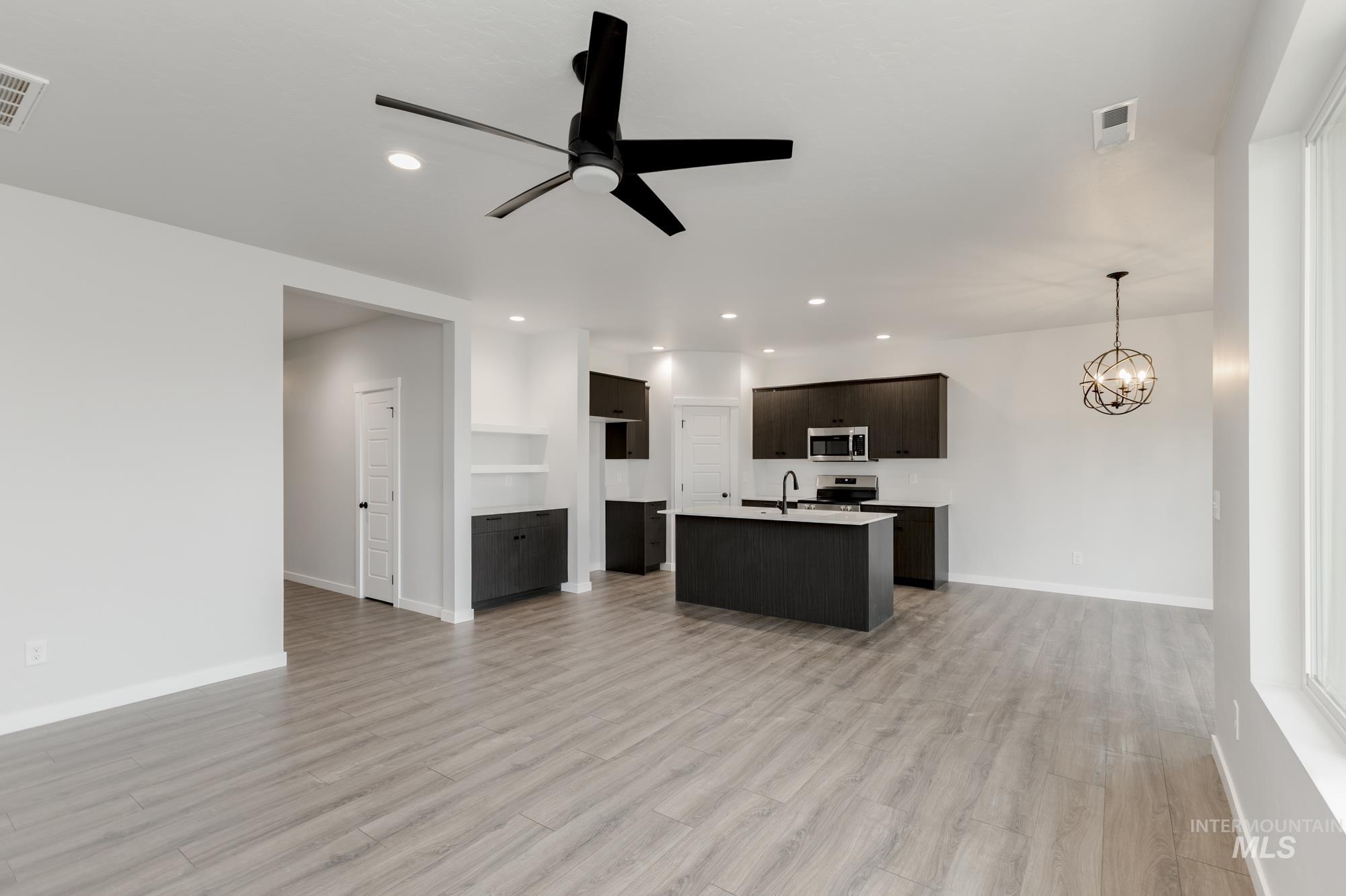 Kitchen featuring stainless steel microwave, open floor plan, ceiling fan, a kitchen island with sink, and light wood-style floors