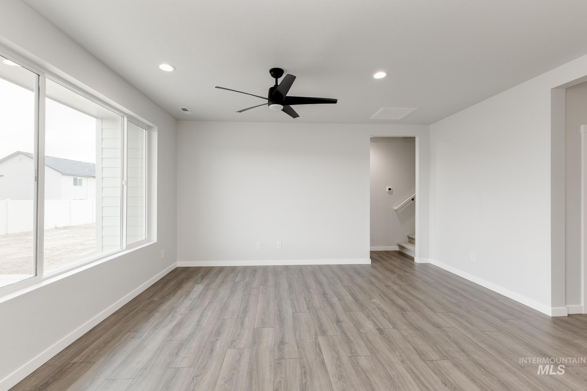 Empty room featuring light wood-type flooring, recessed lighting, ceiling fan, and stairway