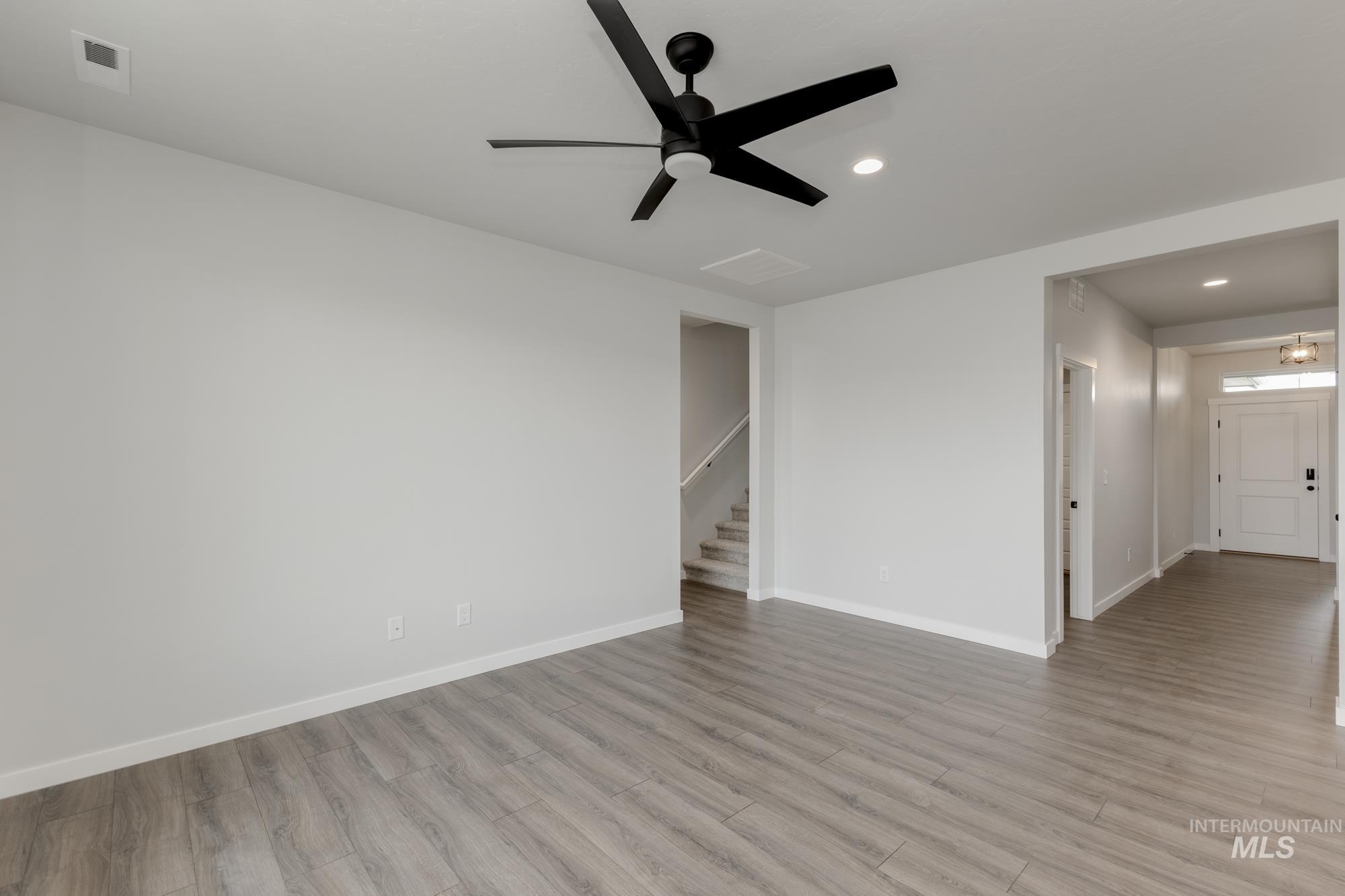 Unfurnished room featuring light wood finished floors, ceiling fan, recessed lighting, and stairway