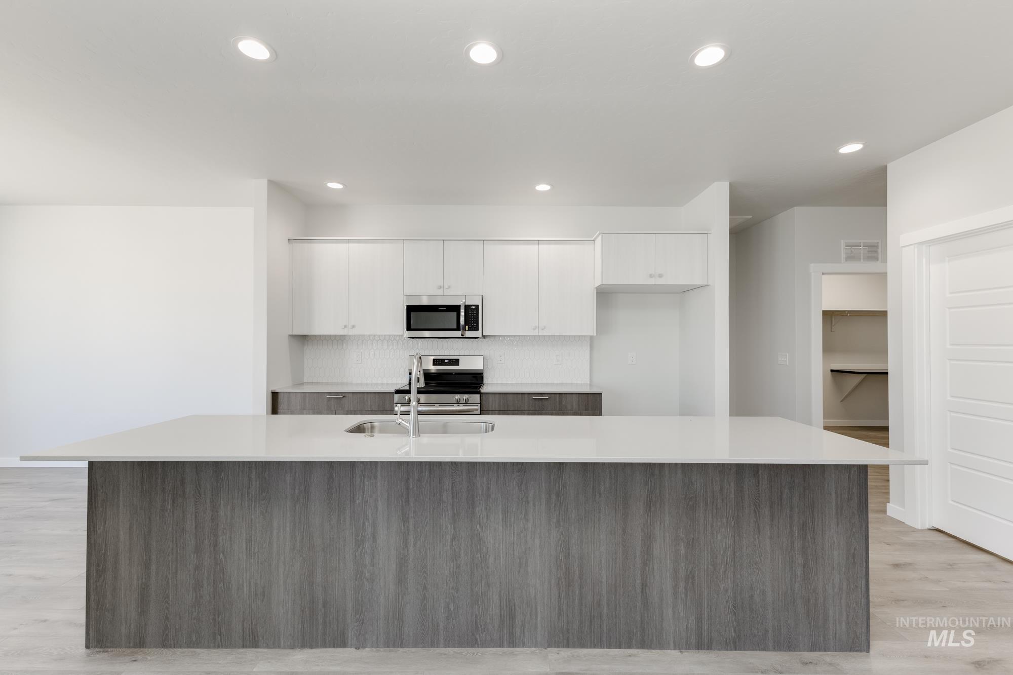Kitchen featuring appliances with stainless steel finishes, white cabinets, a spacious island, decorative backsplash, and light countertops