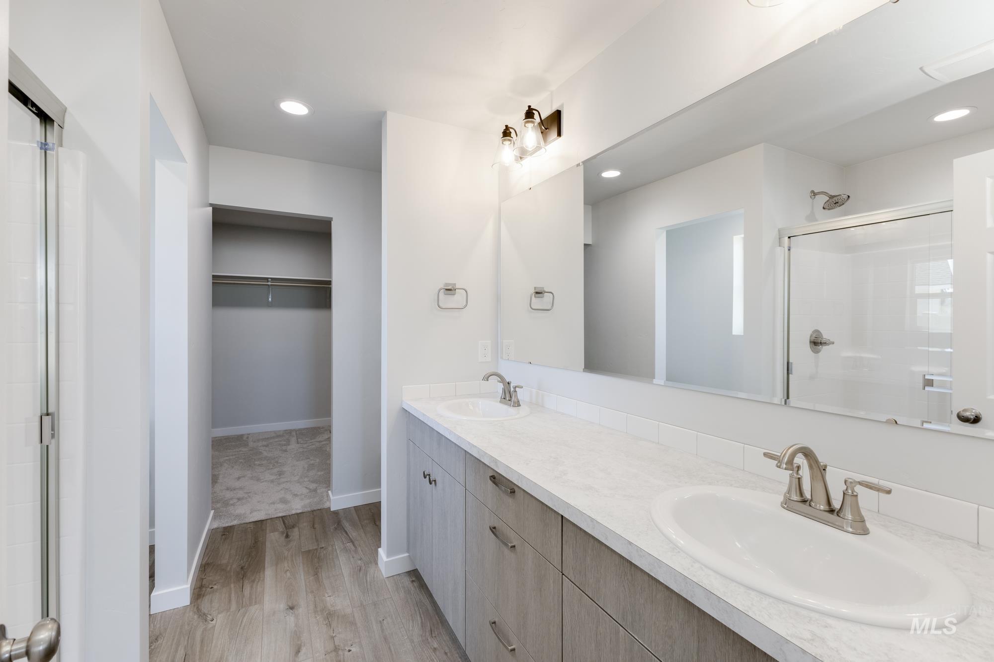 Bathroom featuring a stall shower, double vanity, a spacious closet, recessed lighting, and light wood-style floors
