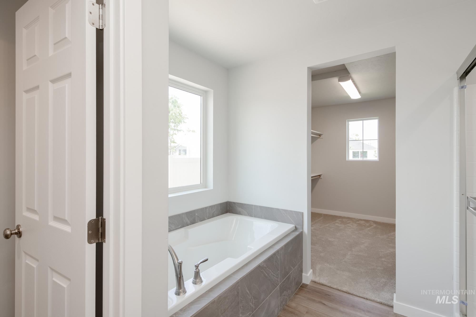 Full bathroom featuring a garden tub, plenty of natural light, and wood finished floors