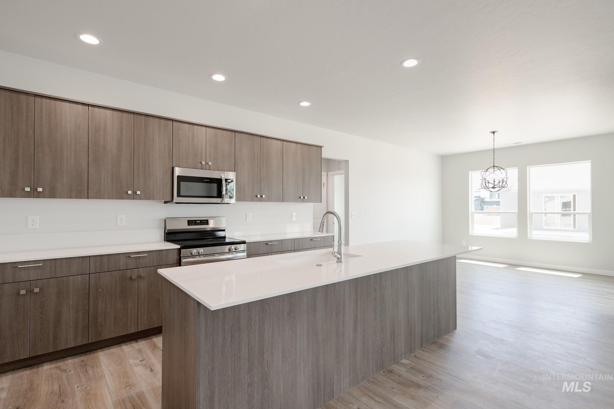 Kitchen with appliances with stainless steel finishes, light countertops, a chandelier, light wood-style floors, and a kitchen island with sink