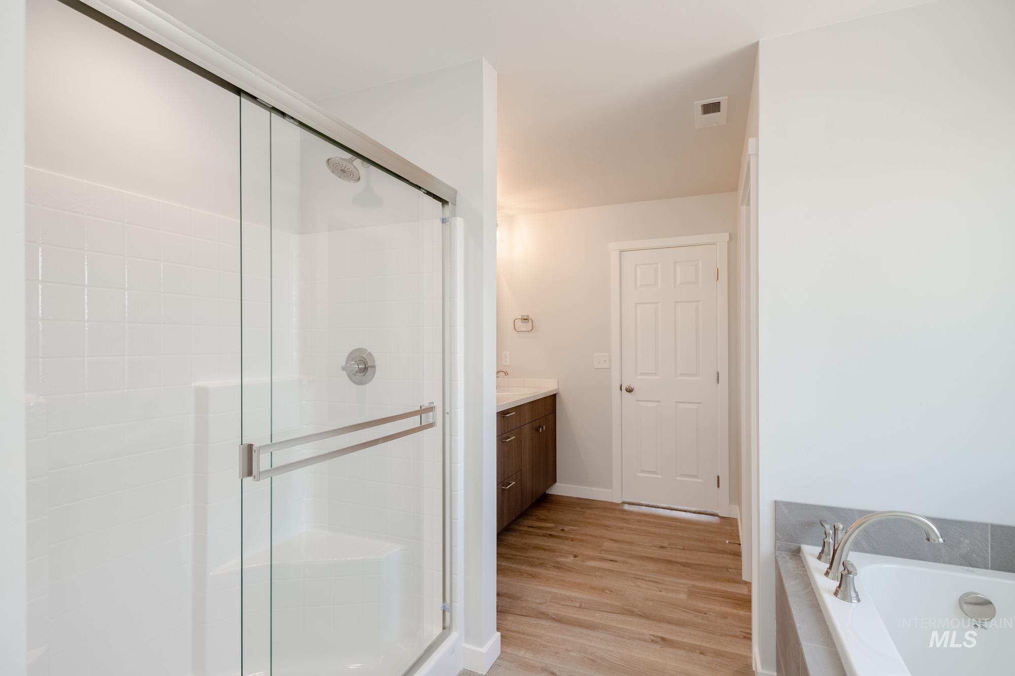 Full bath featuring a shower stall, a bath, vanity, and wood finished floors