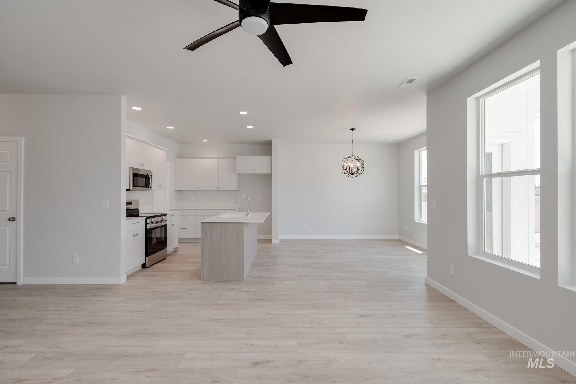 Kitchen with appliances with stainless steel finishes, open floor plan, a chandelier, white cabinets, and recessed lighting