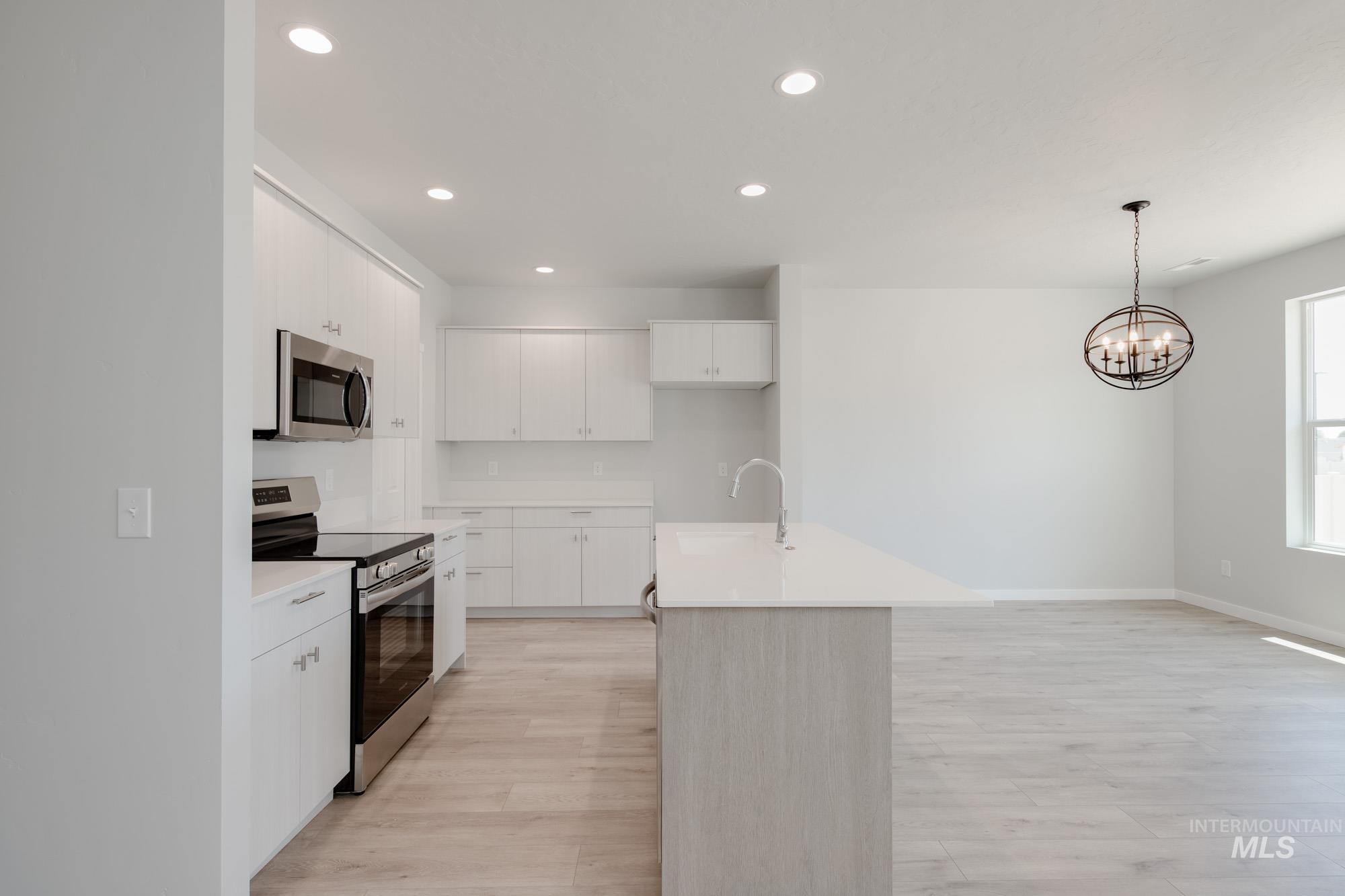 Kitchen featuring stainless steel appliances, light wood-style floors, light countertops, recessed lighting, and decorative light fixtures