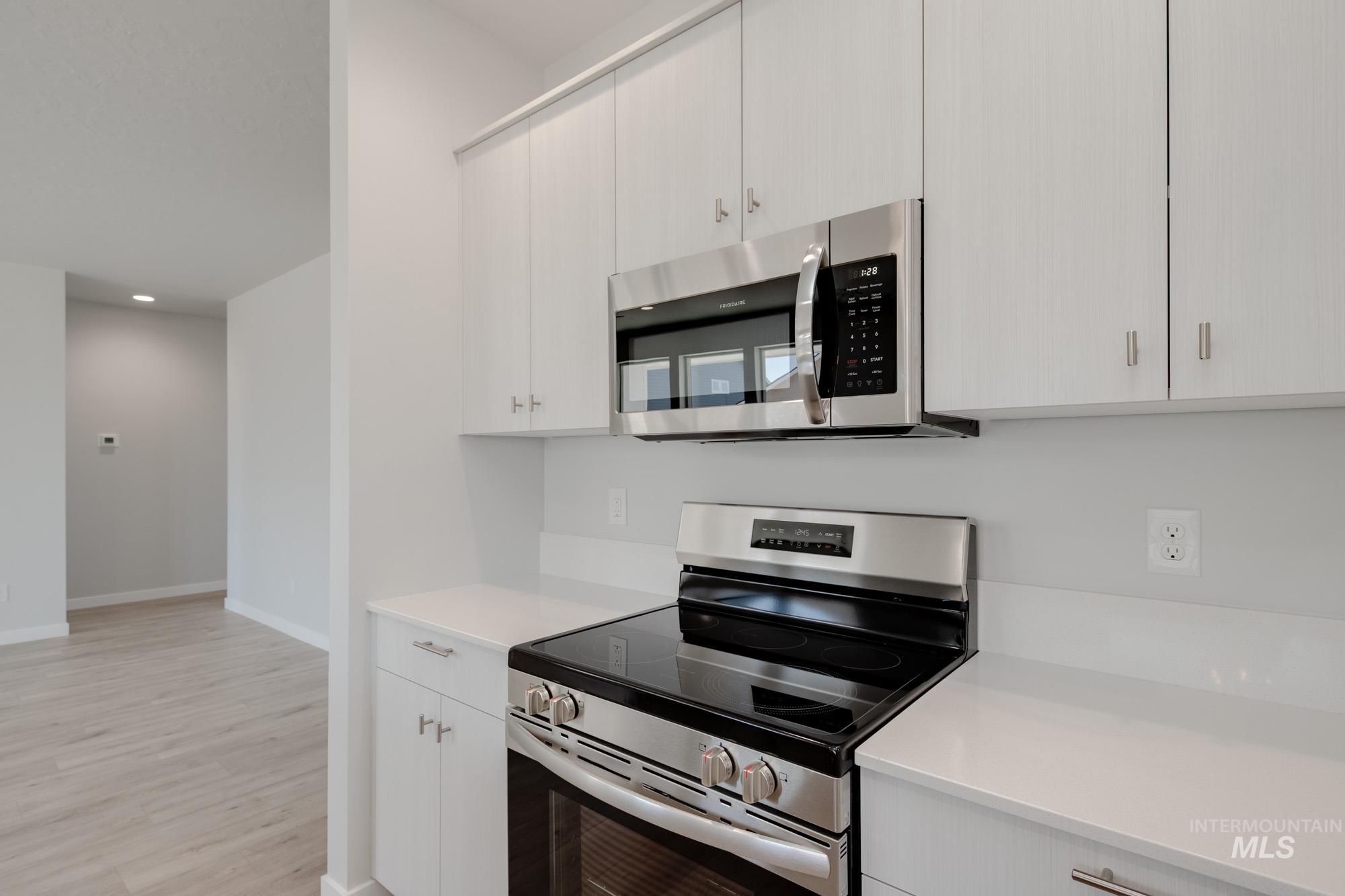 Kitchen with stainless steel appliances, light countertops, light wood-type flooring, recessed lighting, and white cabinetry